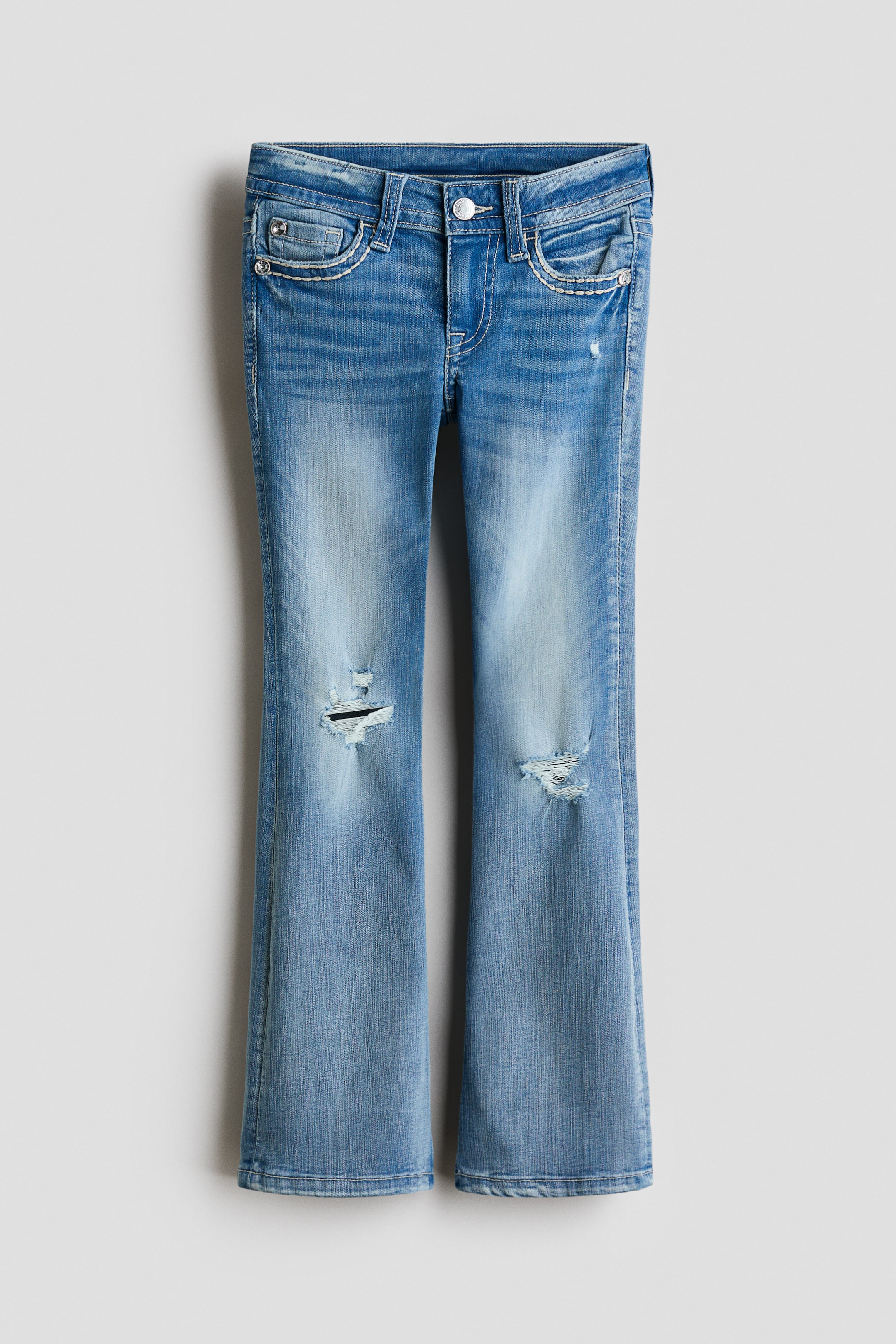 Grotere afbeelding bekijken: Een paar lichtblauwe flared jeans wordt van voren getoond, met scheuren op beide dijen, vervaging en witte contraststiksels die de voorzakken detailleren.