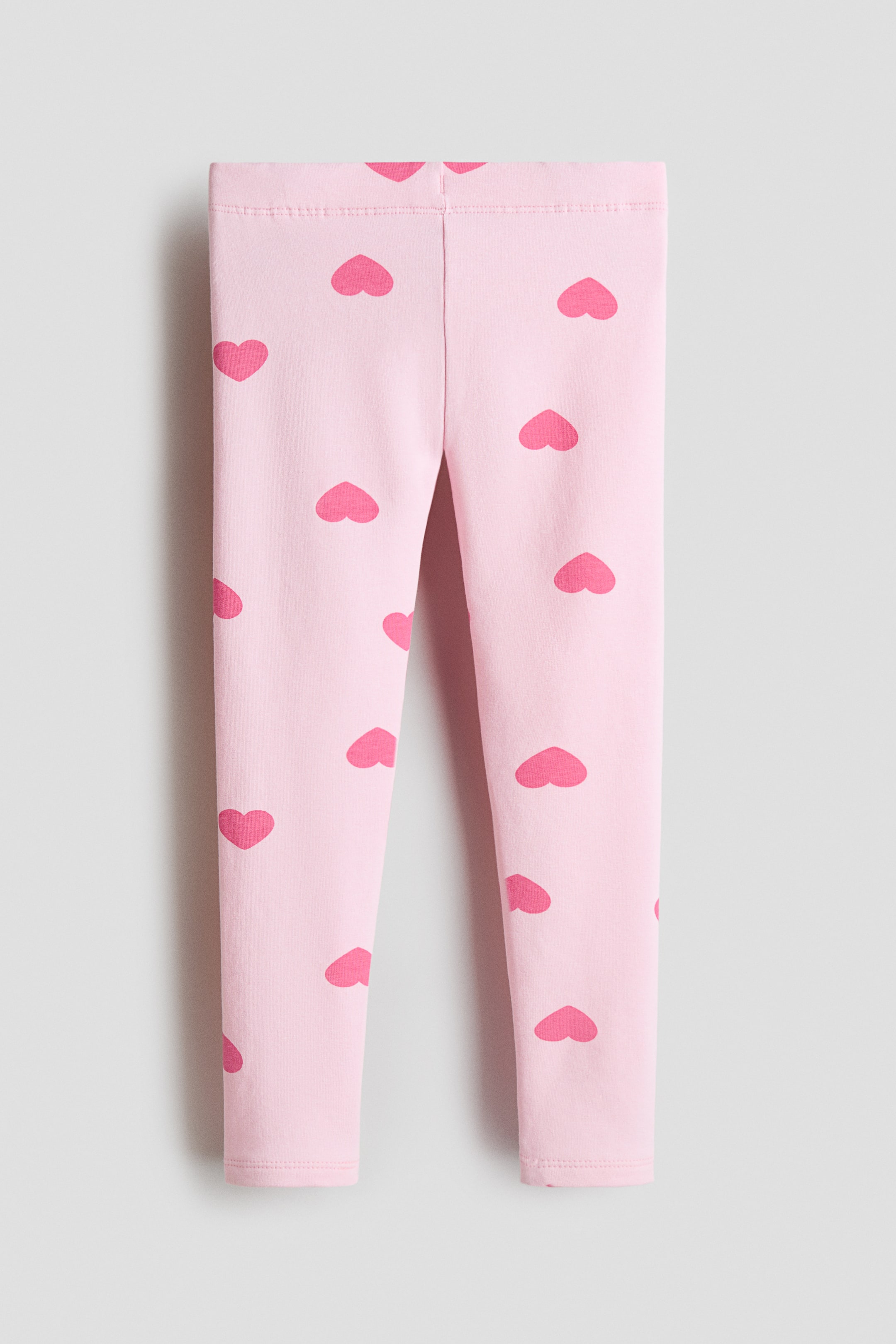 Ver imagen más grande: Los leggings presentan el FRENTE, con una base rosa claro adornada con corazones rosa oscuro dispersos. En la parte superior se ve una cinturilla elástica, y las piernas se extienden hasta el largo completo.