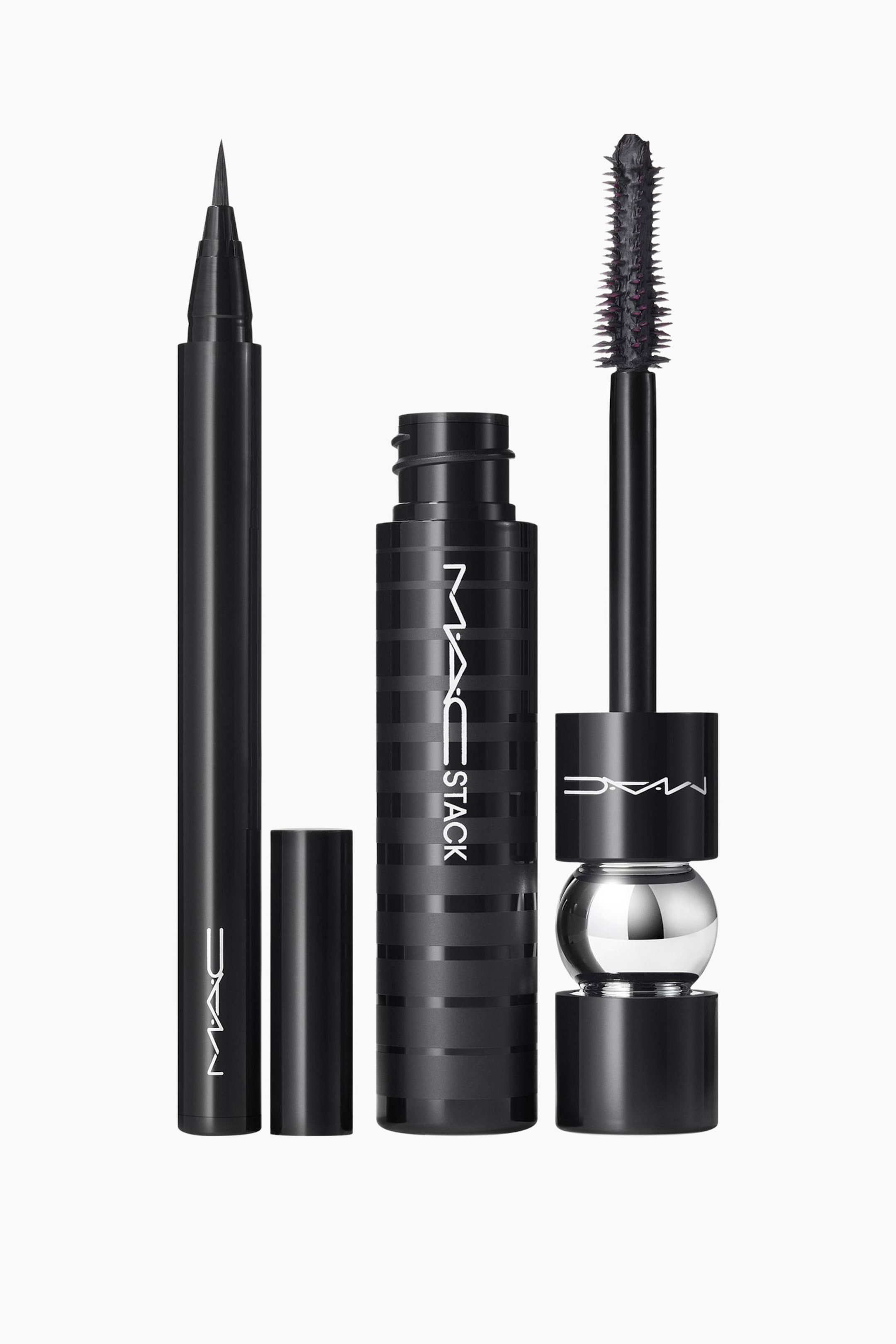 Se større billede: En sort eyeliner-pen står oprejst og viser sin fine spidse spids, med hætten liggende ved siden af. Også oprejst står en sort mascaratube med vandrette striber og "MAC STACK" branding, samt en mascarabørste med en pigget børste og et sort håndtag dekoreret med en sølvkugle.