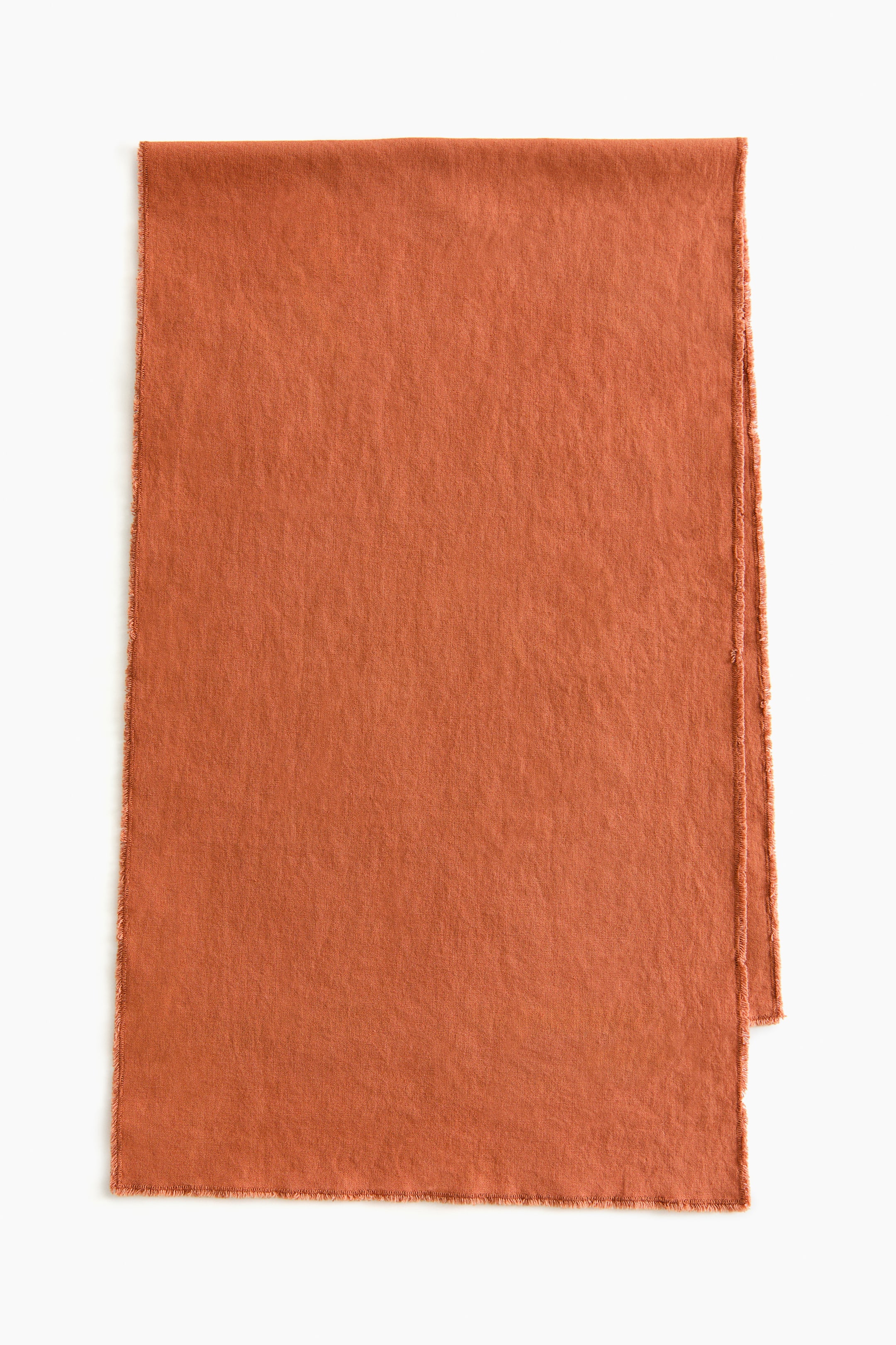 拡大画像を表示: バーントオレンジのテーブルランナーは、リネンとコットンの織りでさりげないテクスチャーがあり、縁全体にフリンジがあしらわれています。