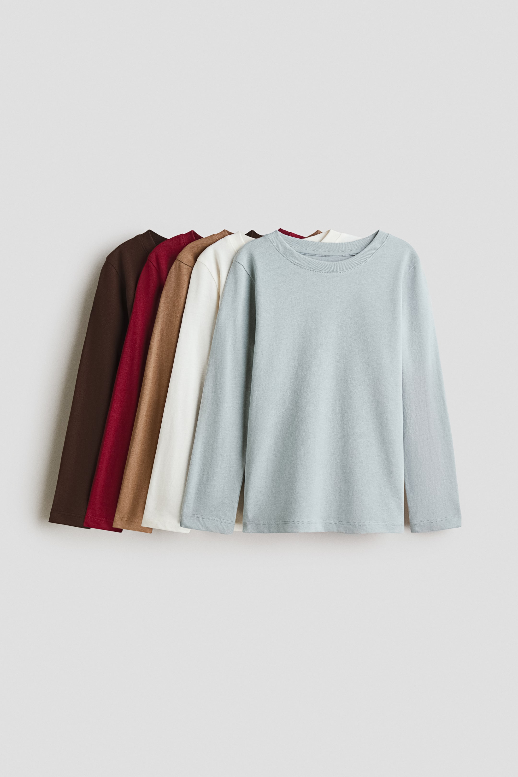 Grotere afbeelding bekijken: Vijf tops met lange mouwen zijn van voren gepresenteerd en in lagen over elkaar gelegd. Deze zachte tops van katoenen jersey hebben een ronde halslijn met een smalle bies, met zichtbare kleuren zoals lichtblauw, crème, tan, donkerrood en bruin.