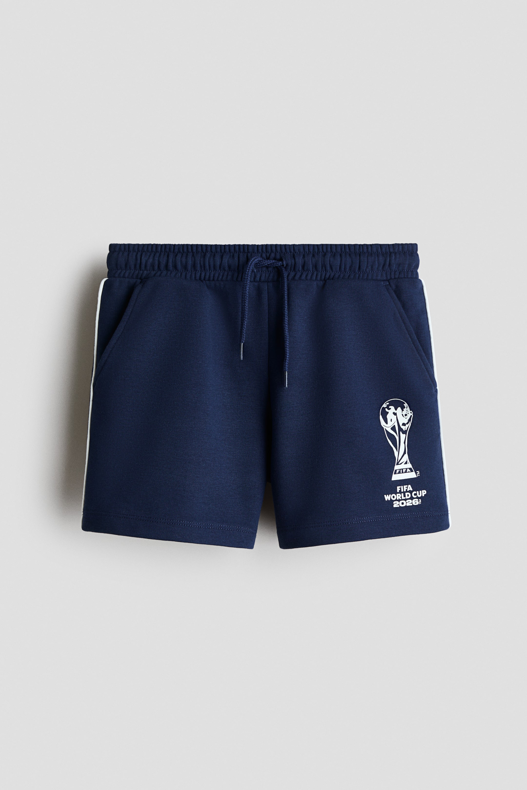 View larger image: Navy blue shorts featuring an elasticated waistband with a drawstring closure. They display two side pockets, a white stripe running down each outer leg, and a white FIFA World Cup 2026! trophy graphic on the lower right leg.