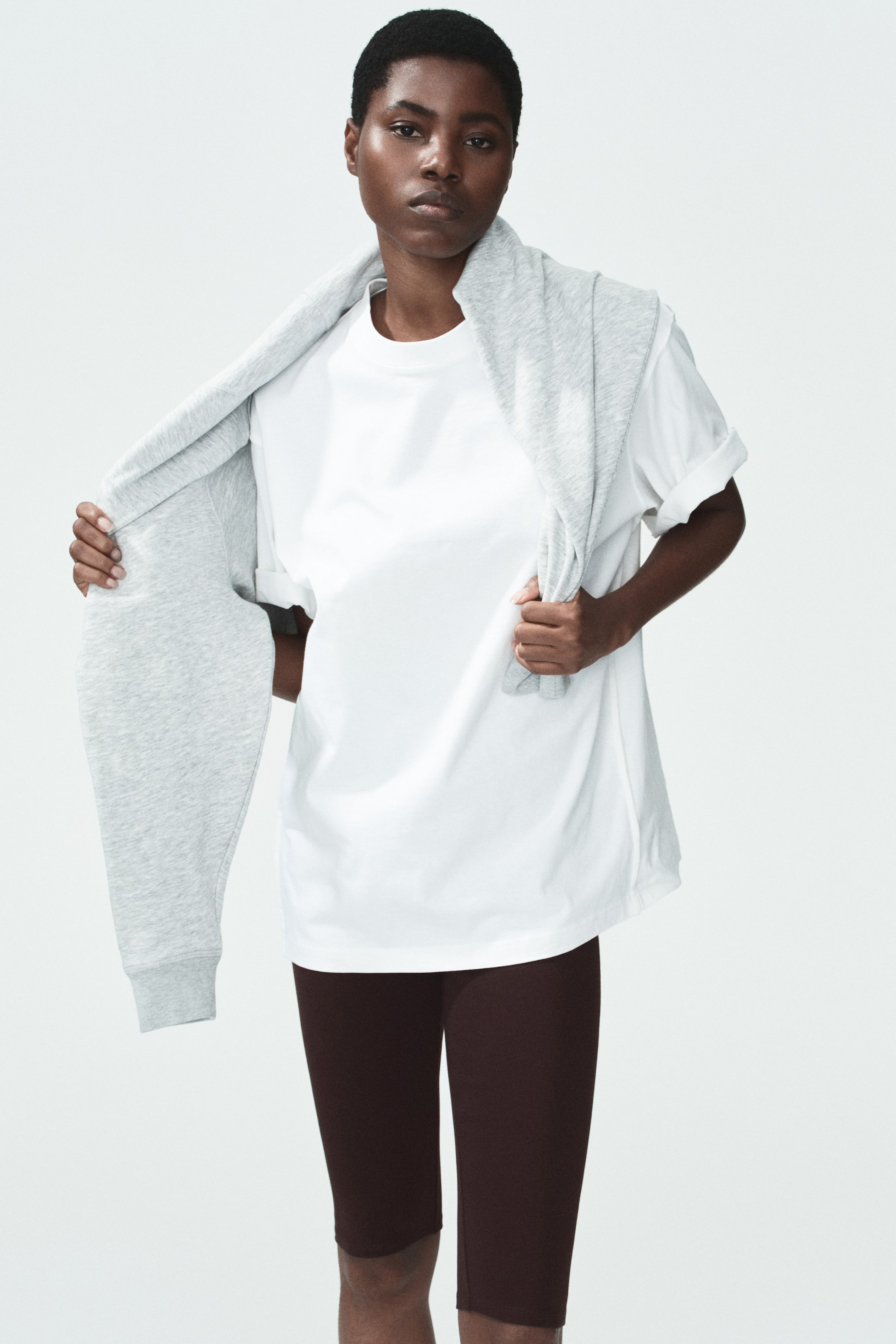 View larger image: Model sedang memakai legging 3/4 panjang dalam warna coklat gelap dari kain kapas lembut, yang memanjang hingga sedikit bawah lutut. Model juga memakai t-shirt putih.