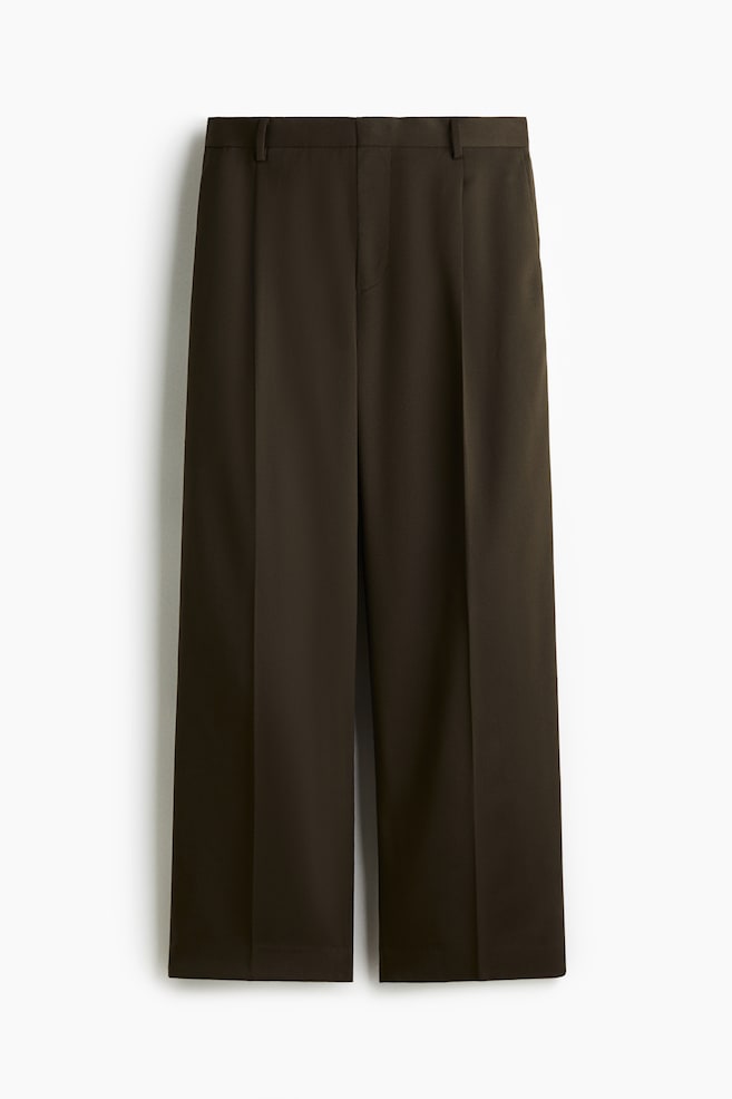 Un par de pantalones de pierna ancha en color marrón oscuro se presenta desde el frente, con una pretina plana con trabillas para cinturón, una bragueta con cremallera oculta y dos pliegues prominentes en cada pierna que se extienden en pliegues marcados hasta el dobladillo recortado. - 1