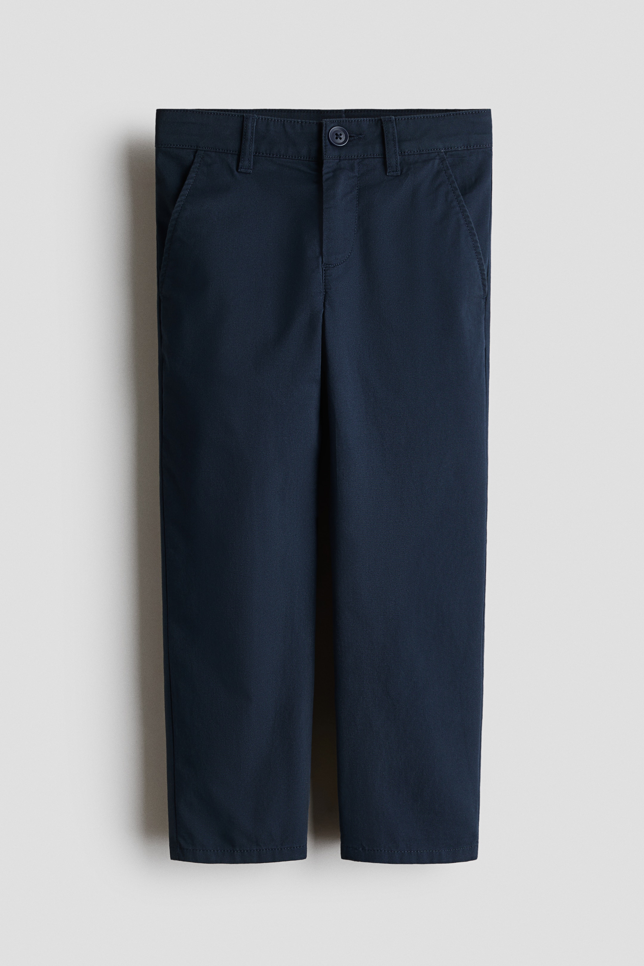 הצגת תמונה גדולה יותר: מכנסי צ'ינו כחול כהה עשויים כותנה טוויל מציגים גזרה רגילה מקדימה, עם סגירת כפתור מעל רוכסן, כיסים צדדיים אלכסוניים ורגליים המתחדדות בעדינות.