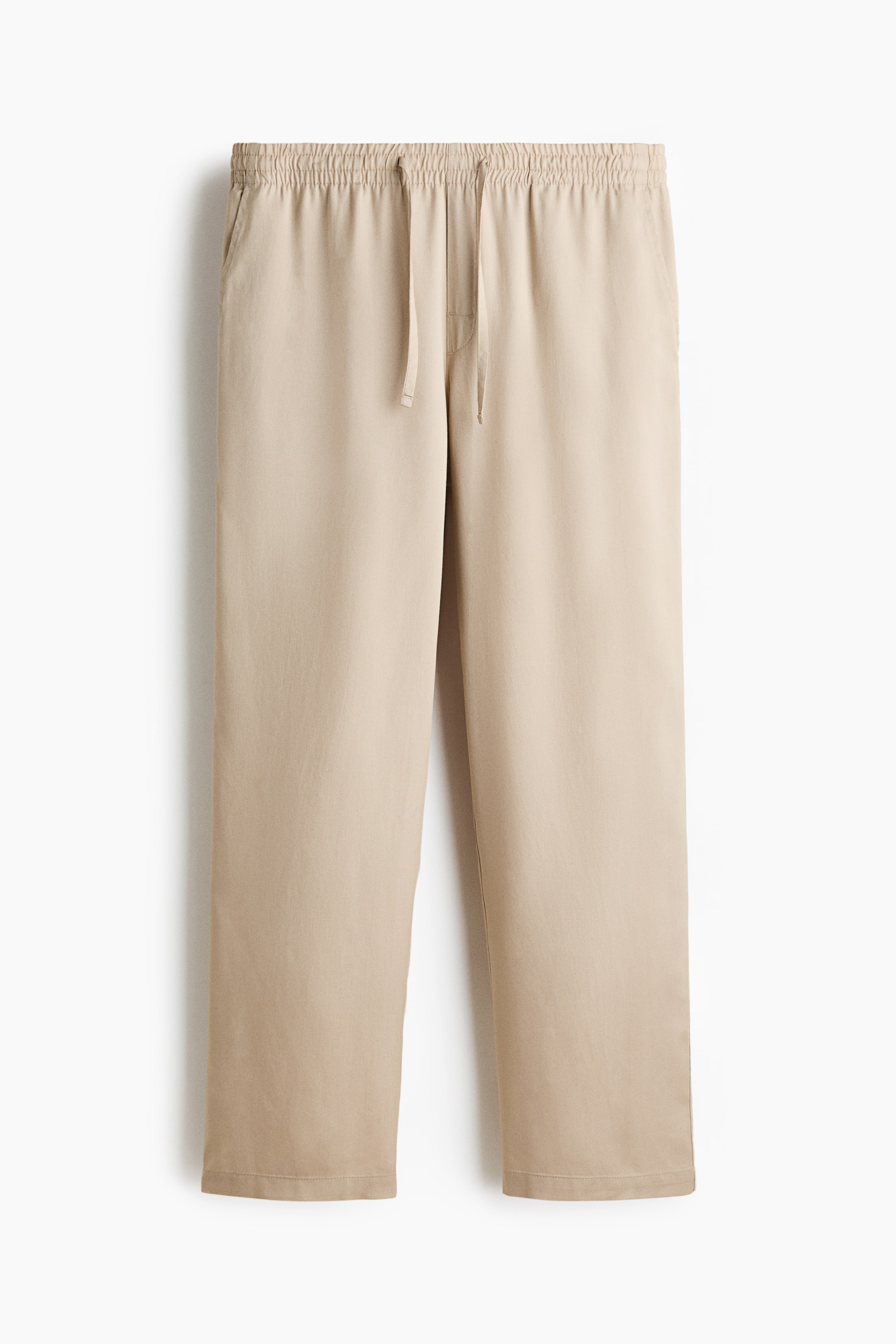 Visa större bild: Byxor visas framifrån, tillverkade i en beige mjuk lyocelljersey. De har en täckt elastisk midja med dragsko, en falsk gylf och öppna sidofickor.