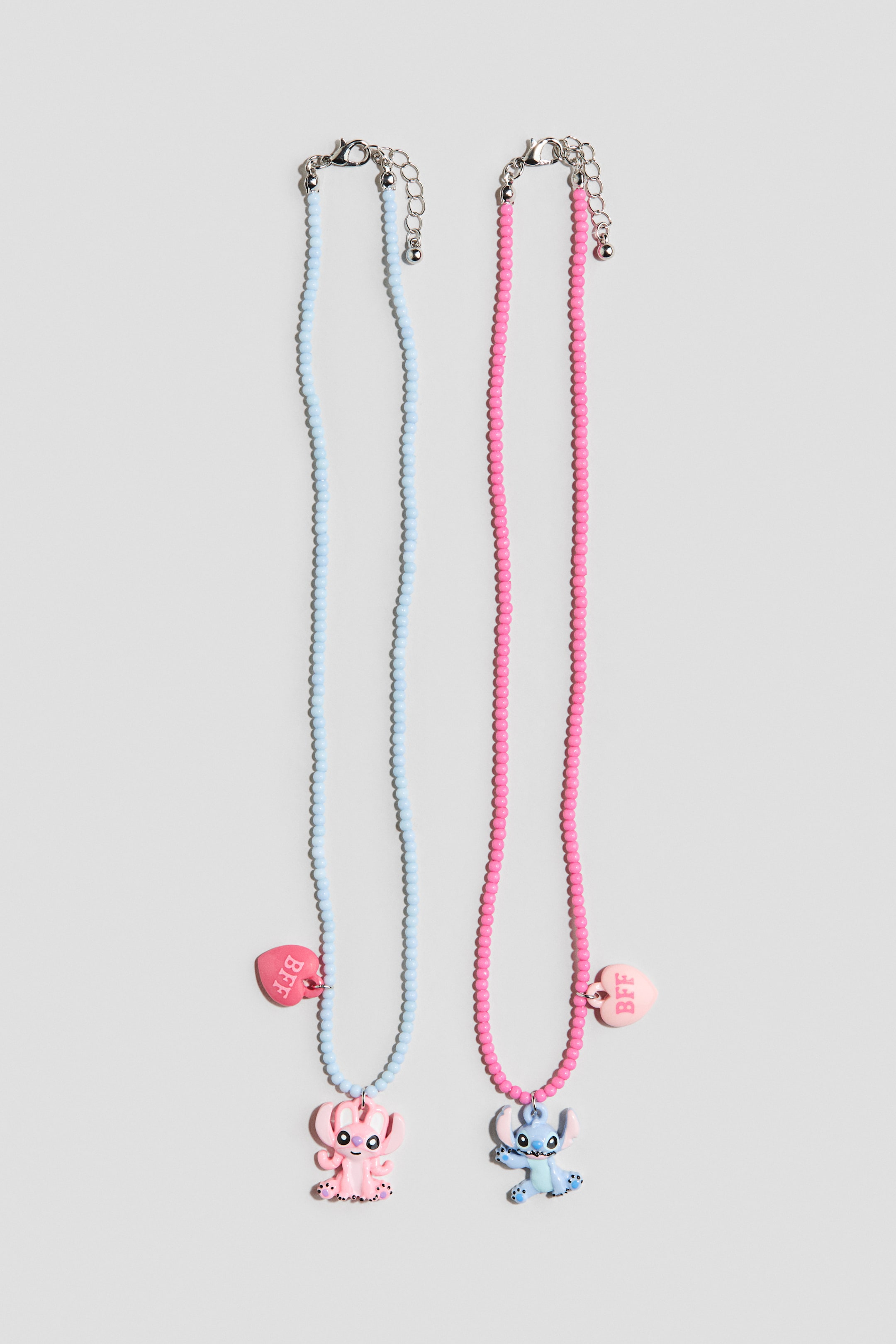 Voir une image plus grande: Deux colliers perlés sont exposés, tous deux dotés de fermoirs ajustables de couleur argentée. Le collier bleu clair présente un pendentif en forme de créature extraterrestre rose avec de grandes oreilles et un pendentif en forme de cœur rose portant le texte "BFF", tous orientés vers l'AVANT. Le collier rose présente un pendentif en forme de créature extraterrestre bleue avec de grandes oreilles et un pendentif en forme de cœur rose pâle portant le texte "BFF", tous orientés vers l'AVANT.