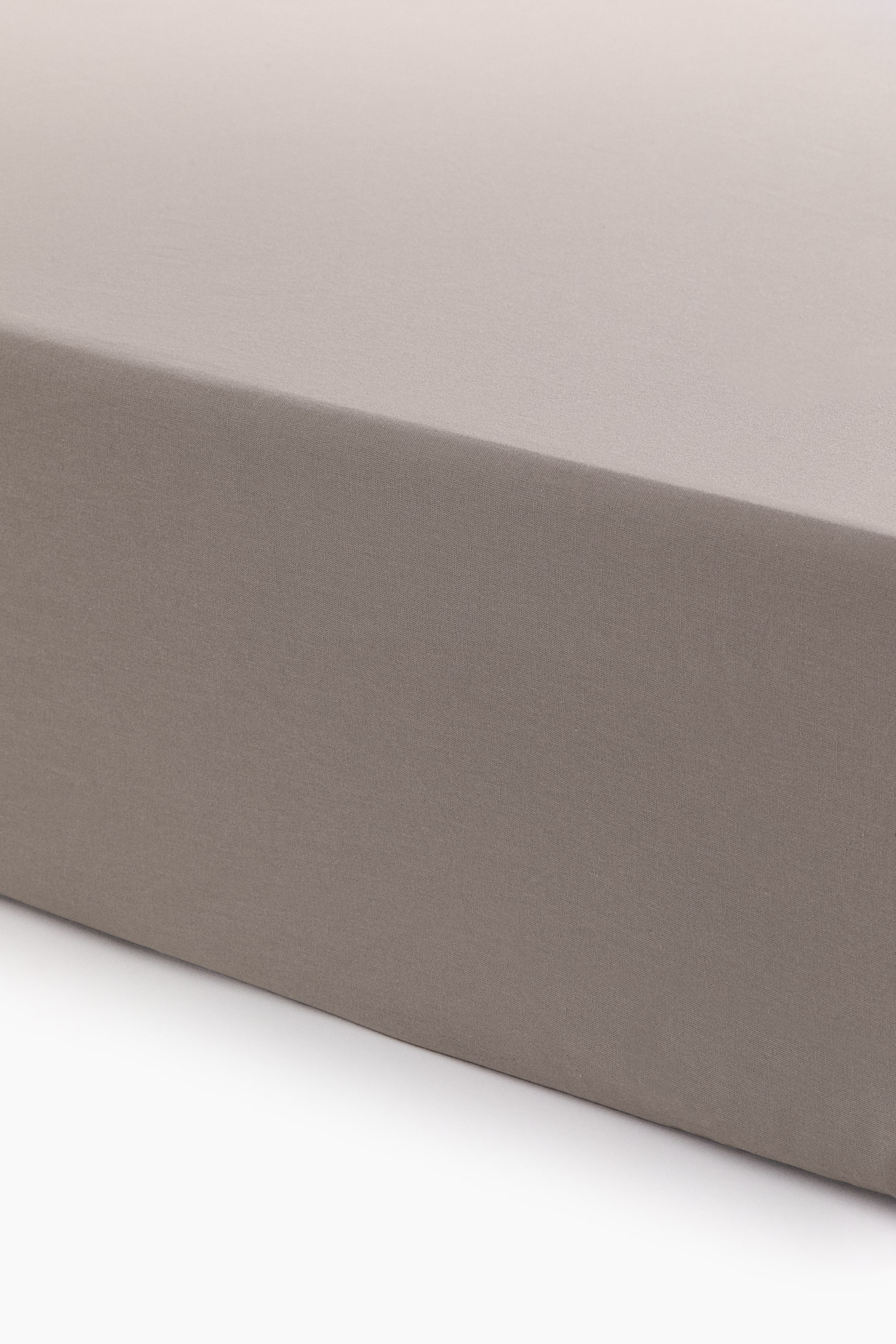 View larger image: A taupe fitted sheet stretches over a rectangular shape, showcasing its smooth top surface and vertical side from a front-right perspective.
