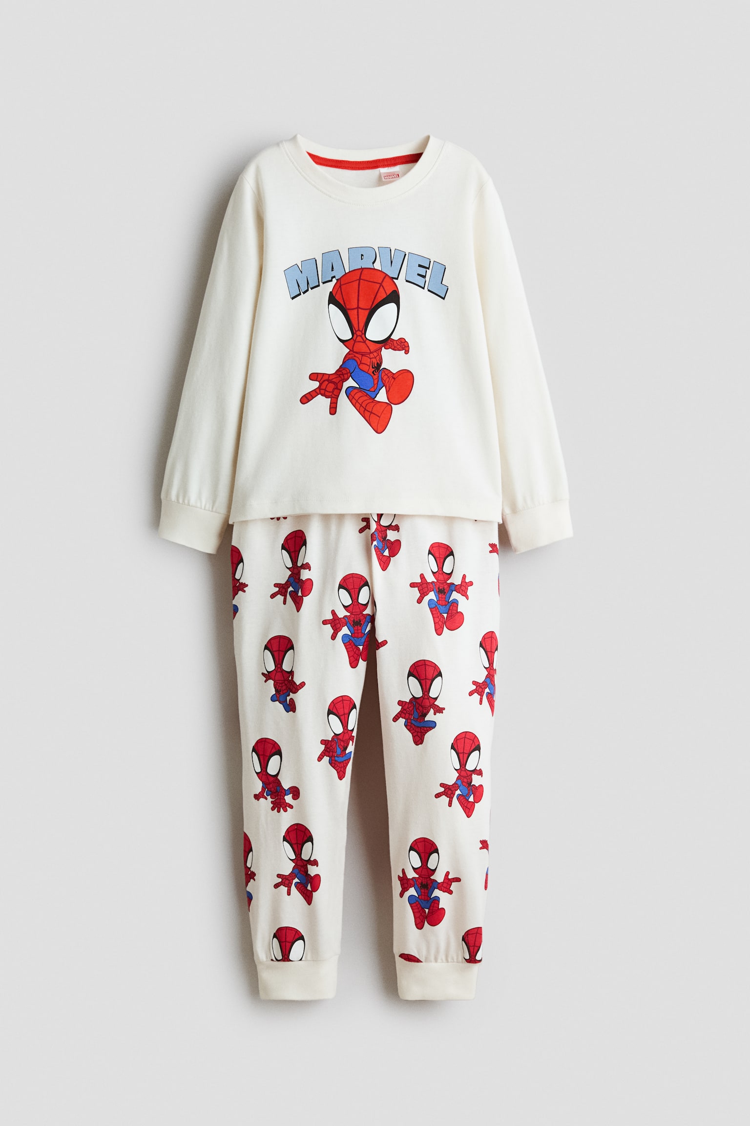 Ekru renkte iki parÃ§alÄ± bir pijama takÄ±mÄ± Ã¶nden gÃ¶sterilmektedir; uzun kollu bir Ã¼st ve uyumlu bir alt parÃ§adan oluÅur. Ãstte, mavi "MARVEL" yazÄ±sÄ±nÄ±n altÄ±nda yer alan merkezi bir Ã§izgi film Spiderman gÃ¶rseli, fitilli yuvarlak yaka ve manÅetlerle birlikte sunulurken; pantolonda her yere yayÄ±lan Spiderman deseni ve fitilli paÃ§alar bulunmaktadÄ±r.