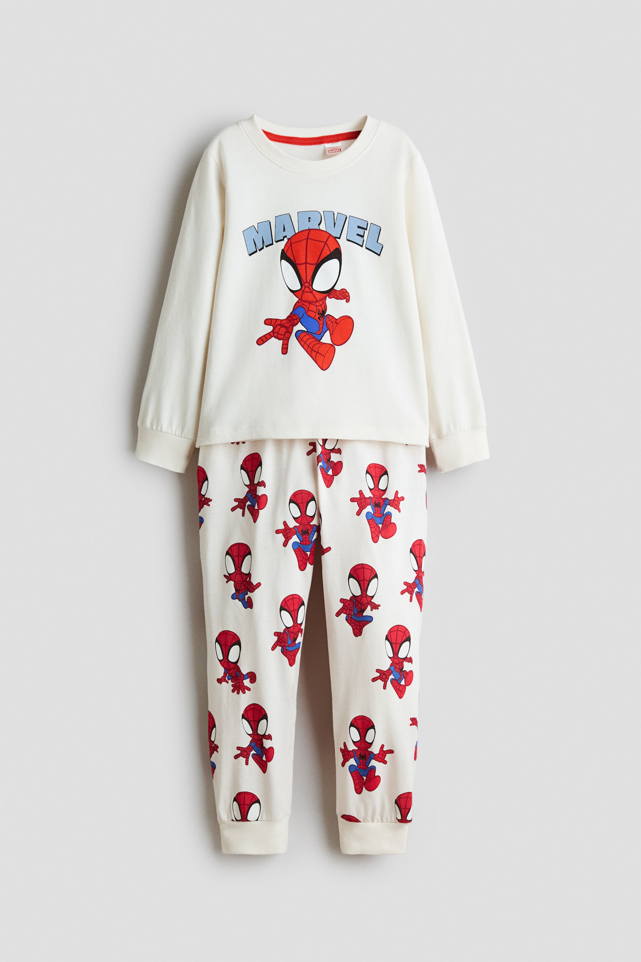 Büyük resmi görüntüle: Ekru renkte iki parçalı bir pijama takımı önden gösterilmektedir; uzun kollu bir üst ve uyumlu bir alt parçadan oluşur. Üstte, mavi "MARVEL" yazısının altında yer alan merkezi bir çizgi film Spiderman görseli, fitilli yuvarlak yaka ve manşetlerle birlikte sunulurken; pantolonda her yere yayılan Spiderman deseni ve fitilli paçalar bulunmaktadır.