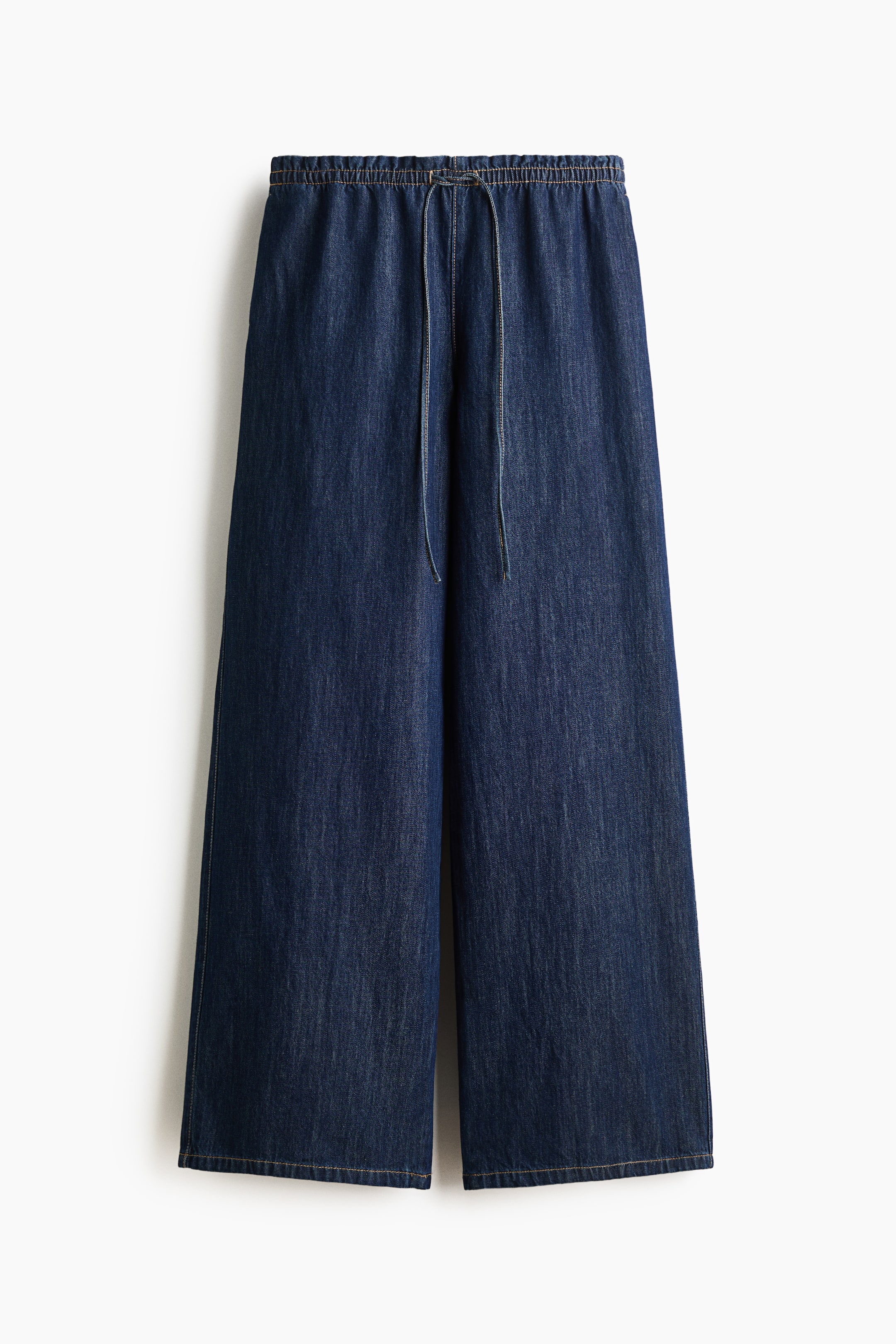 Vezi imaginea mai mare: Pantalonii apar într-un material din denim moale, de culoare albastru închis, prezentați din față. Aceștia sunt prevăzuți cu o talie elastică și un șnur de strângere în centru, fiind croiți cu o siluetă cu picior larg.