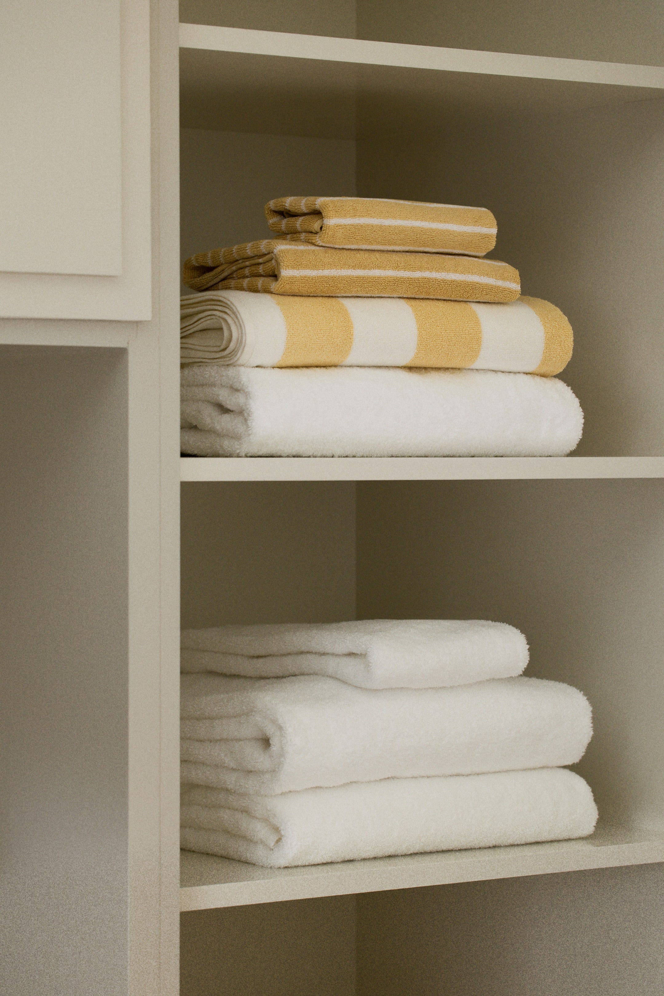 View larger image: Two smaller yellow towels with thin white stripes are placed on a larger white towel with thick yellow stripes, which is set upon a plain white towel, all forming an upper stack. Three plain white towels create a separate lower stack.