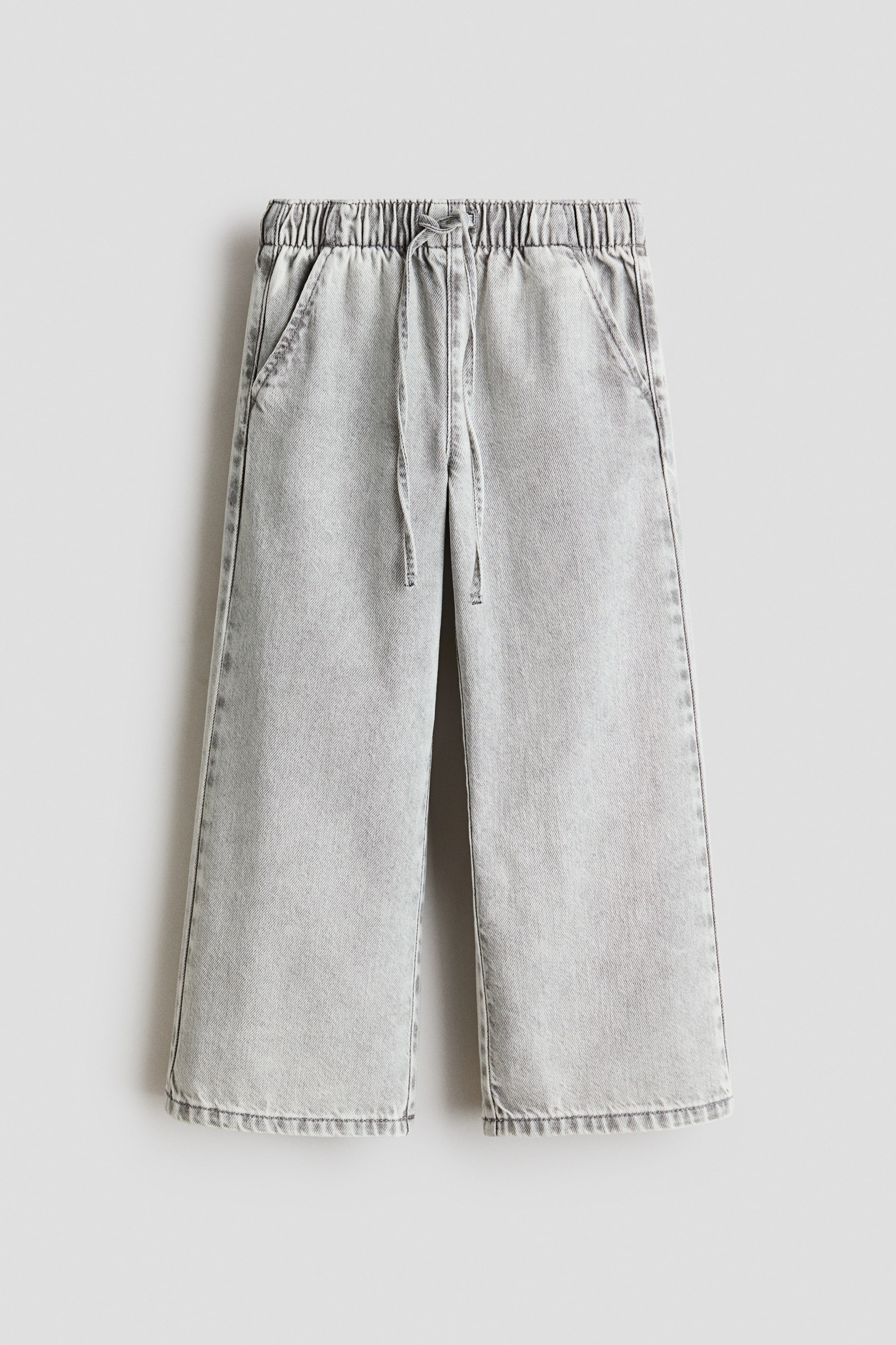 Se større billede: Lysegrå syrevaskede denim bukser med elastisk snøre i taljen og sidelommer. De vide bukser har en kortere længde.