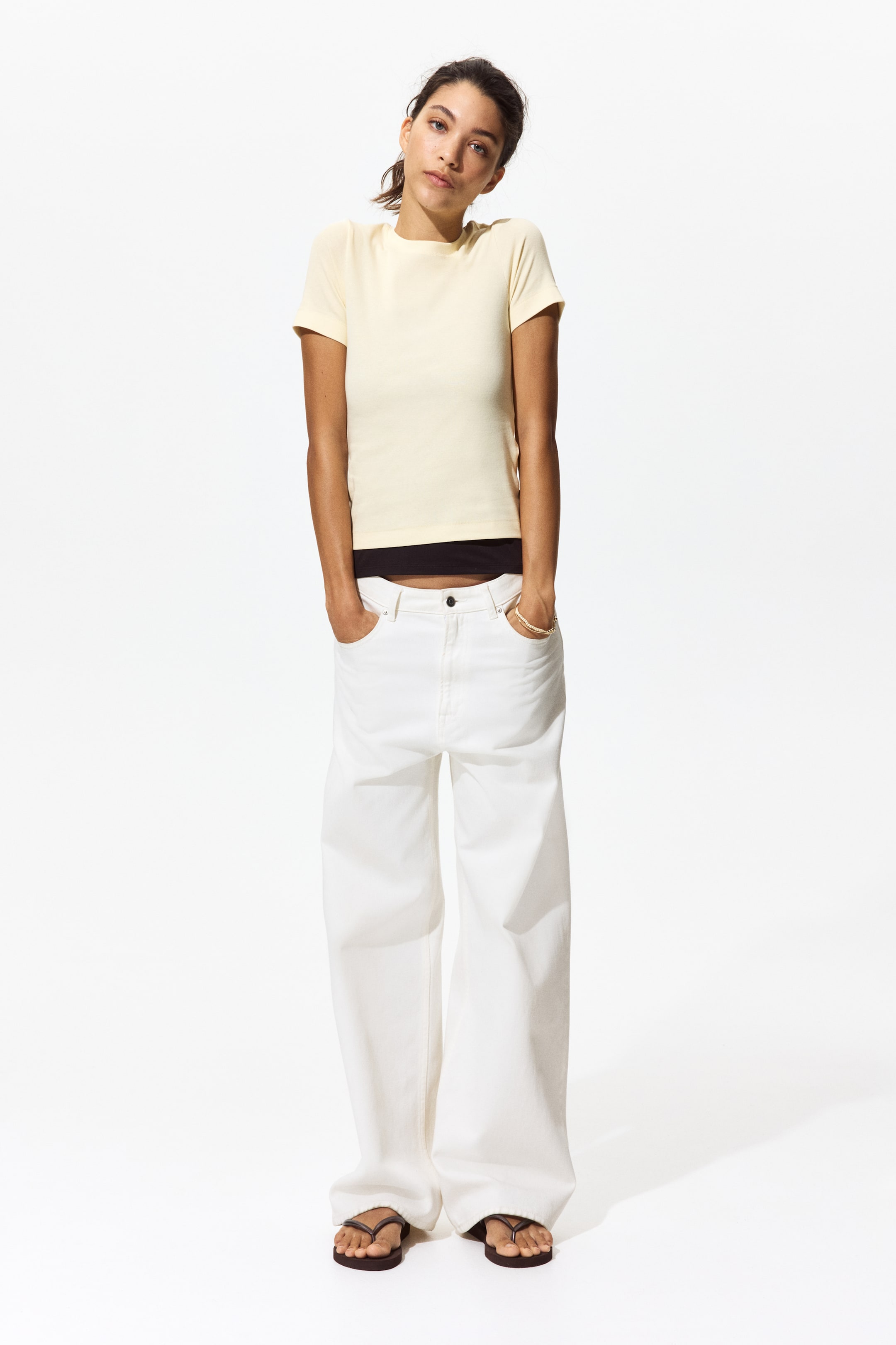 View larger image: A light yellow short-sleeved t-shirt is displayed front-facing, featuring a crew neck and a fitted silhouette. It is layered over a black underlayer, visible at the hem.