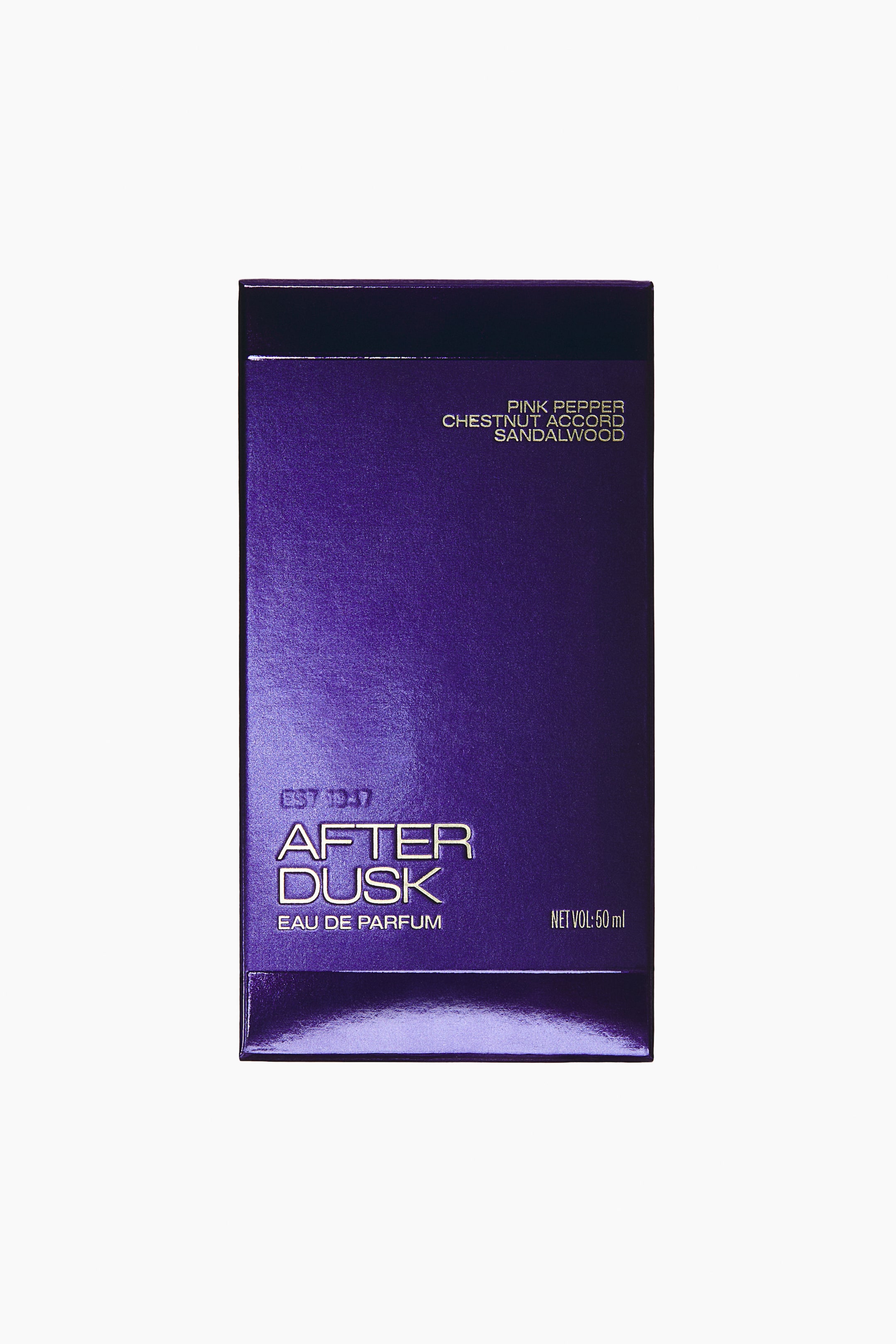 Grotere afbeelding bekijken: Een rechthoekige parfumdoos staat frontaal, met een metallic diep paarse afwerking en gouden letters. Op de doos staan de merkgegevens "EST 1947" en "AFTER DUSK EAU DE PARFUM" in reliëf linksonder, geurnoten rechtsboven vermeld en "NET VOL: 50 ml" rechtsonder.