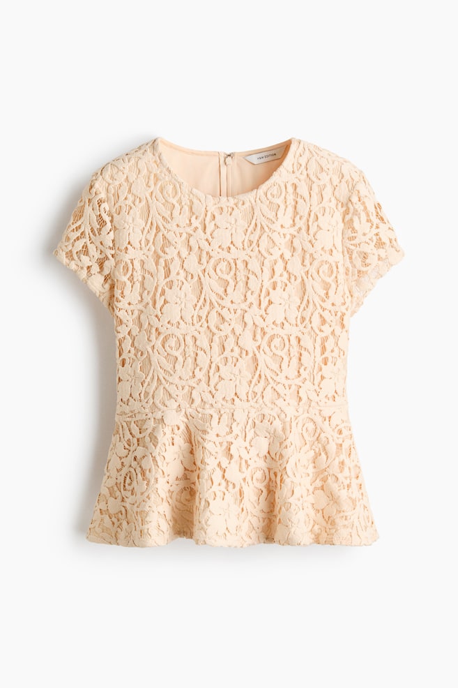 A light peach short-sleeved top, seen from the front, is featuring a delicate floral lace overlay with a solid lining. It is designed with a round neckline, a peplum hem, and a visible zipper closure at the back of the neck. - 1