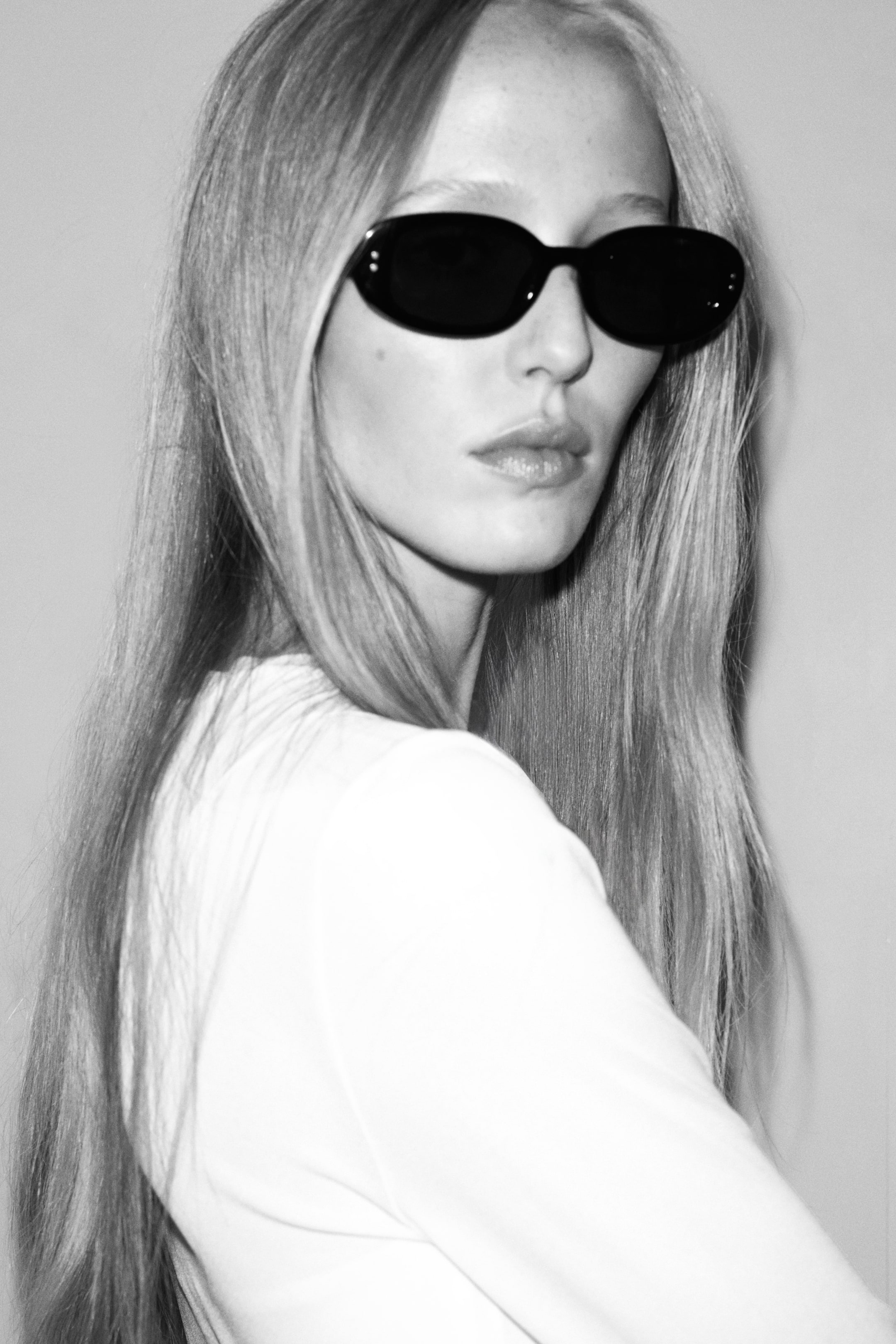 View larger image: Oval sunglasses with dark plastic frames and dark-tinted lenses are being worn by the model, who is also wearing a light-coloured top.