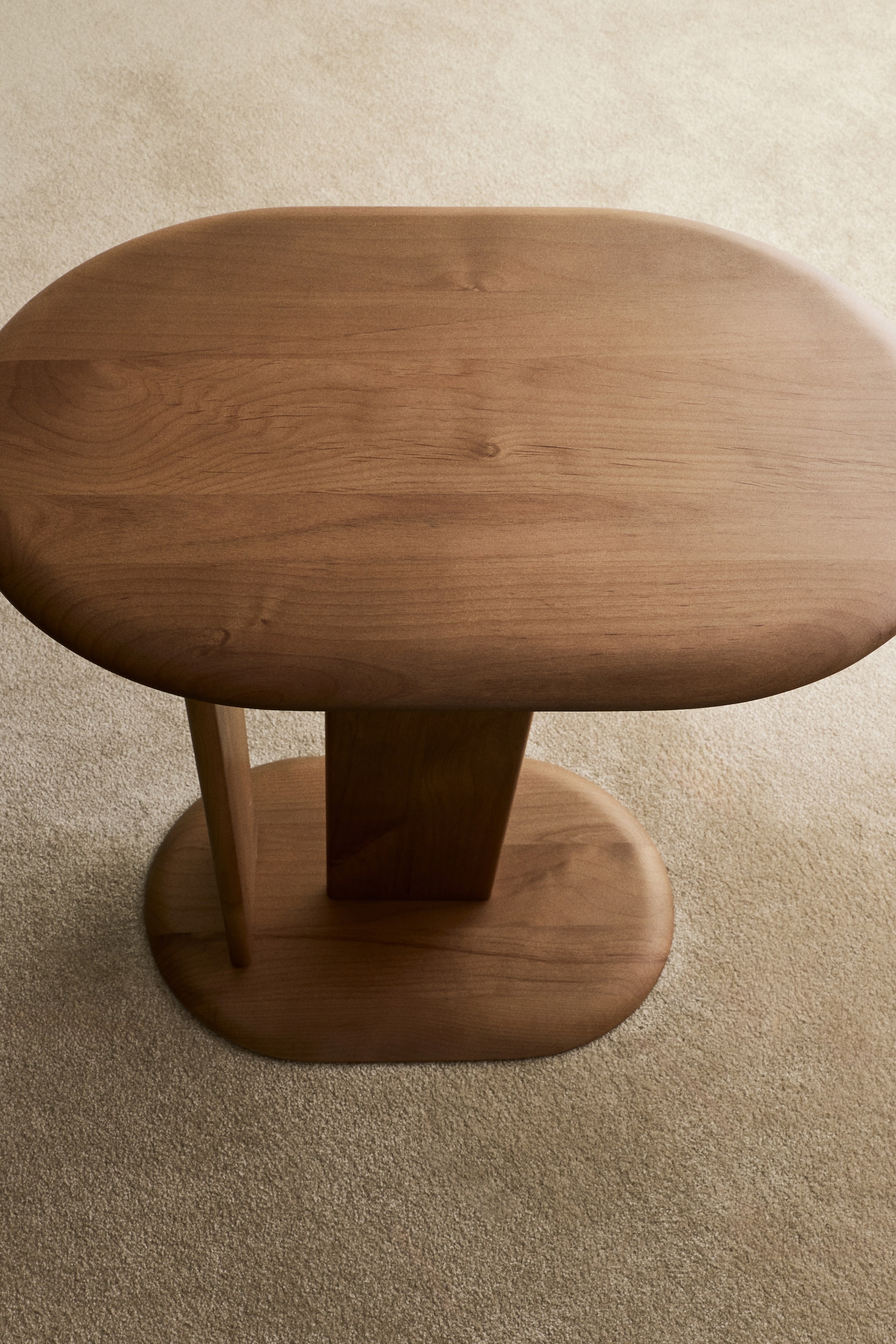 Größeres Bild ansehen: Ein Holztisch präsentiert eine ovale Tischplatte mit sanft gerundeten Kanten. Er wird von einer zentralen rechteckigen Säule und einer zusätzlichen flachen, dünneren Säule getragen, die beide auf einer ovalen Basis ruhen.