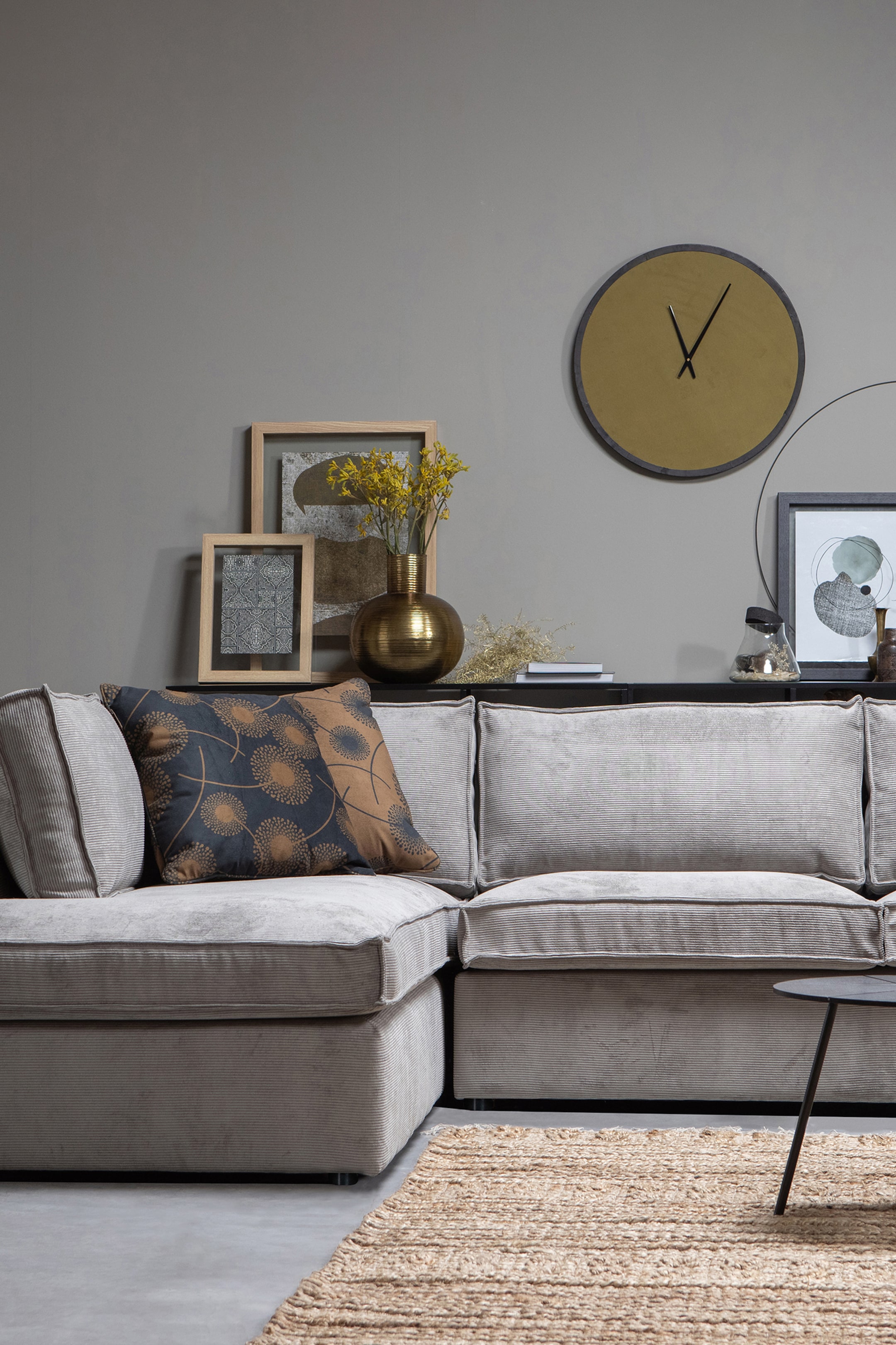 Größeres Bild ansehen: Ein hellgraues Ecksofa bildet eine L-Form und präsentiert einen gerippten Cordstoff. Es verfügt über weiche Sitz- und Rückenkissen mit sichtbaren Paspeln entlang der Kanten, während ein dekoratives Wurfkissen in der Ecke ruht.