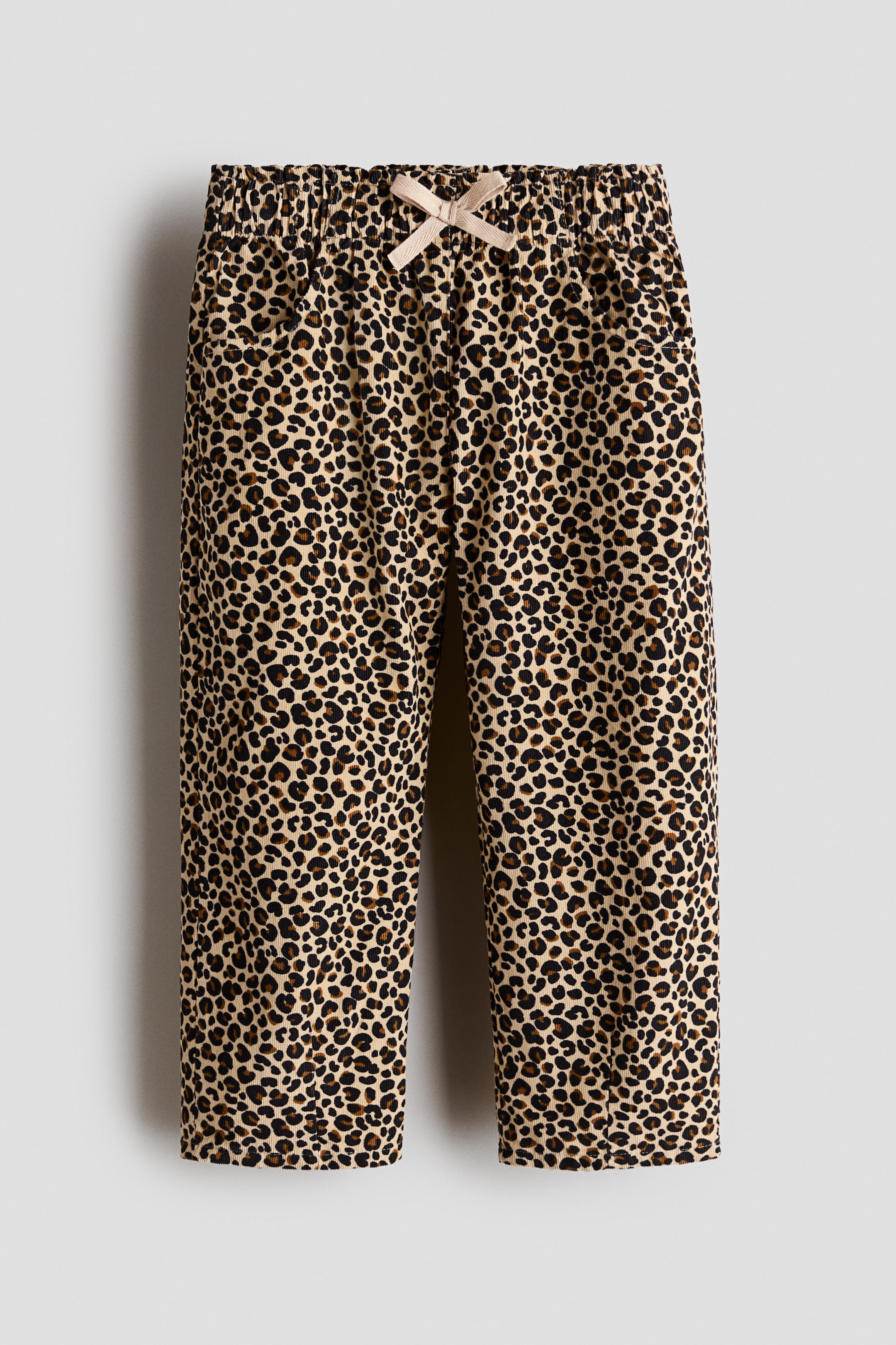 View larger image: A pair of front-facing leopard-print corduroy pants features an elasticated waistband with a light beige decorative bow tied at the centre. The straight-leg trousers show textured vertical ribbing and subtle side pockets.