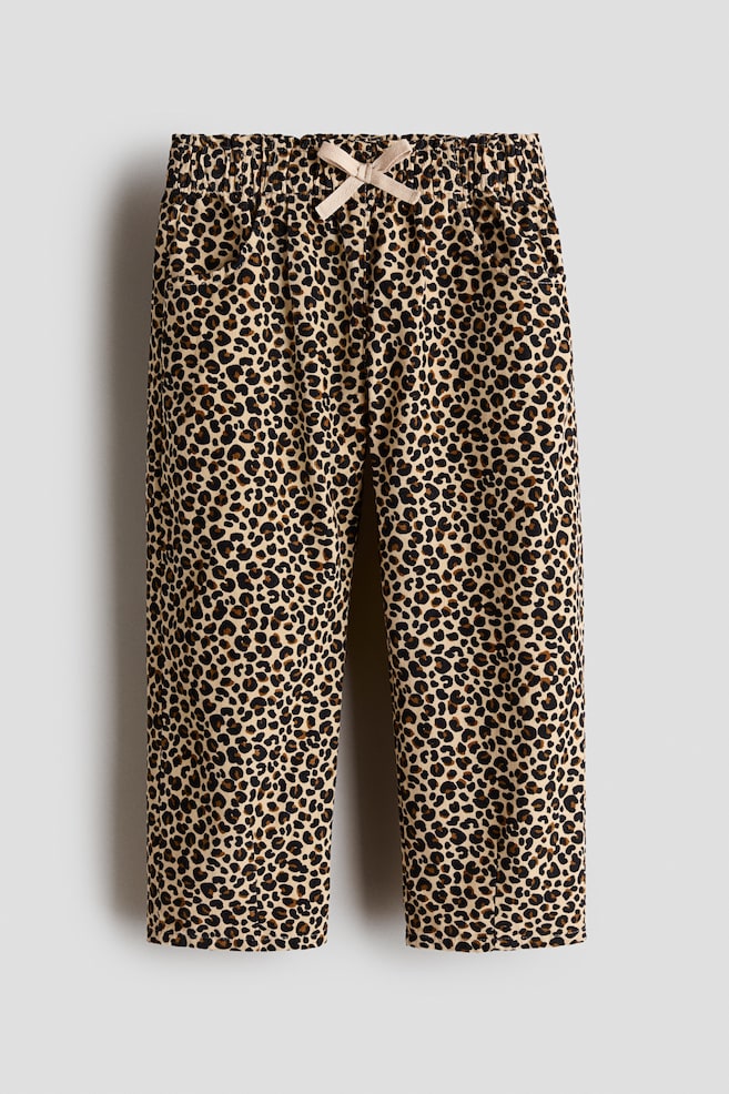 Eine frontale Aufnahme einer Hose mit Leopardenmuster aus Cord mit elastischem Bund, verziert mit einer hellbeigen dekorativen Schleife in der Mitte. Die Hose mit geradem Bein zeigt eine strukturierte vertikale Rippung und dezente Seitentaschen. - 1