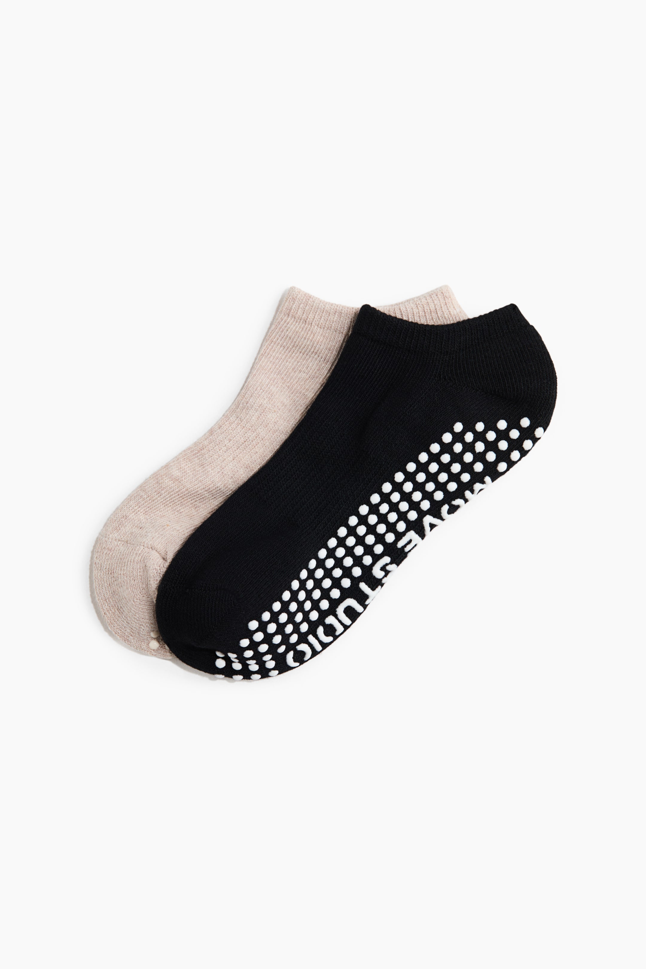 View larger image: A black and a beige fine-knit shaftless sock overlap diagonally, each showcasing subtly ribbed tops and white anti-slip dots across their soles. The black sock's sole also displays the word "STUDIO" crafted from these dots.