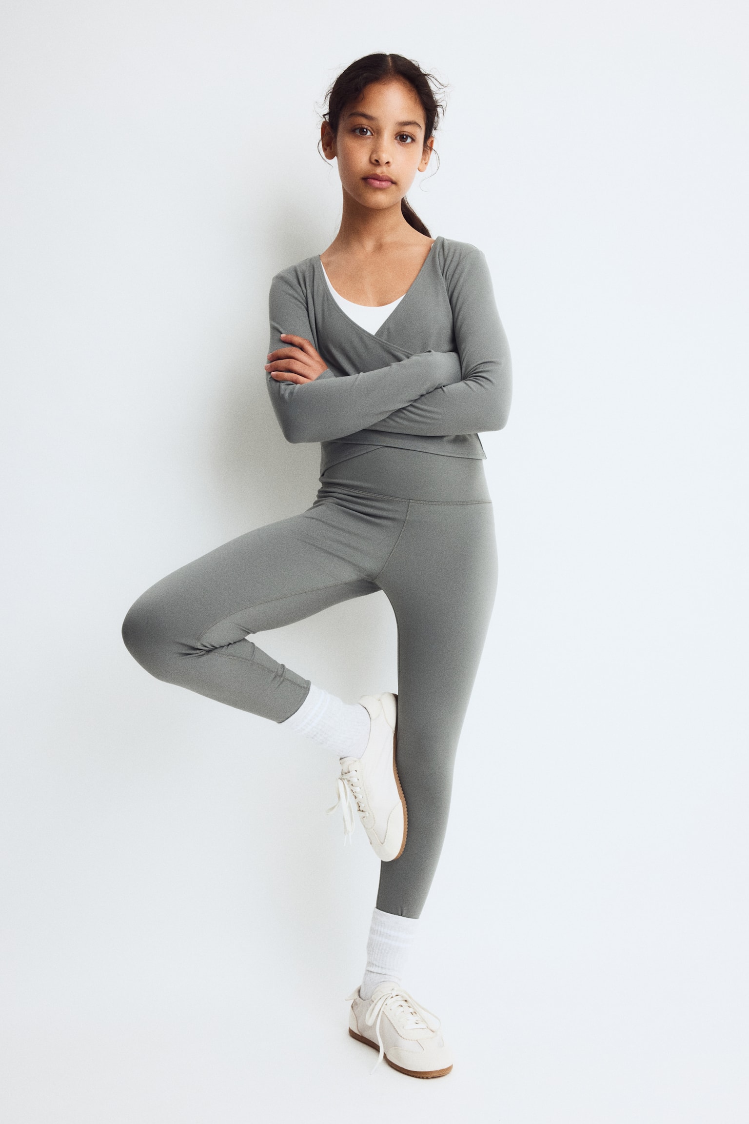 Grey sports leggings are displayed flat, facing forward, showcasing a smooth, matte fabric. They are crafted with a wide high-rise waistband, visible flatlock seams, and a cropped length. - 1