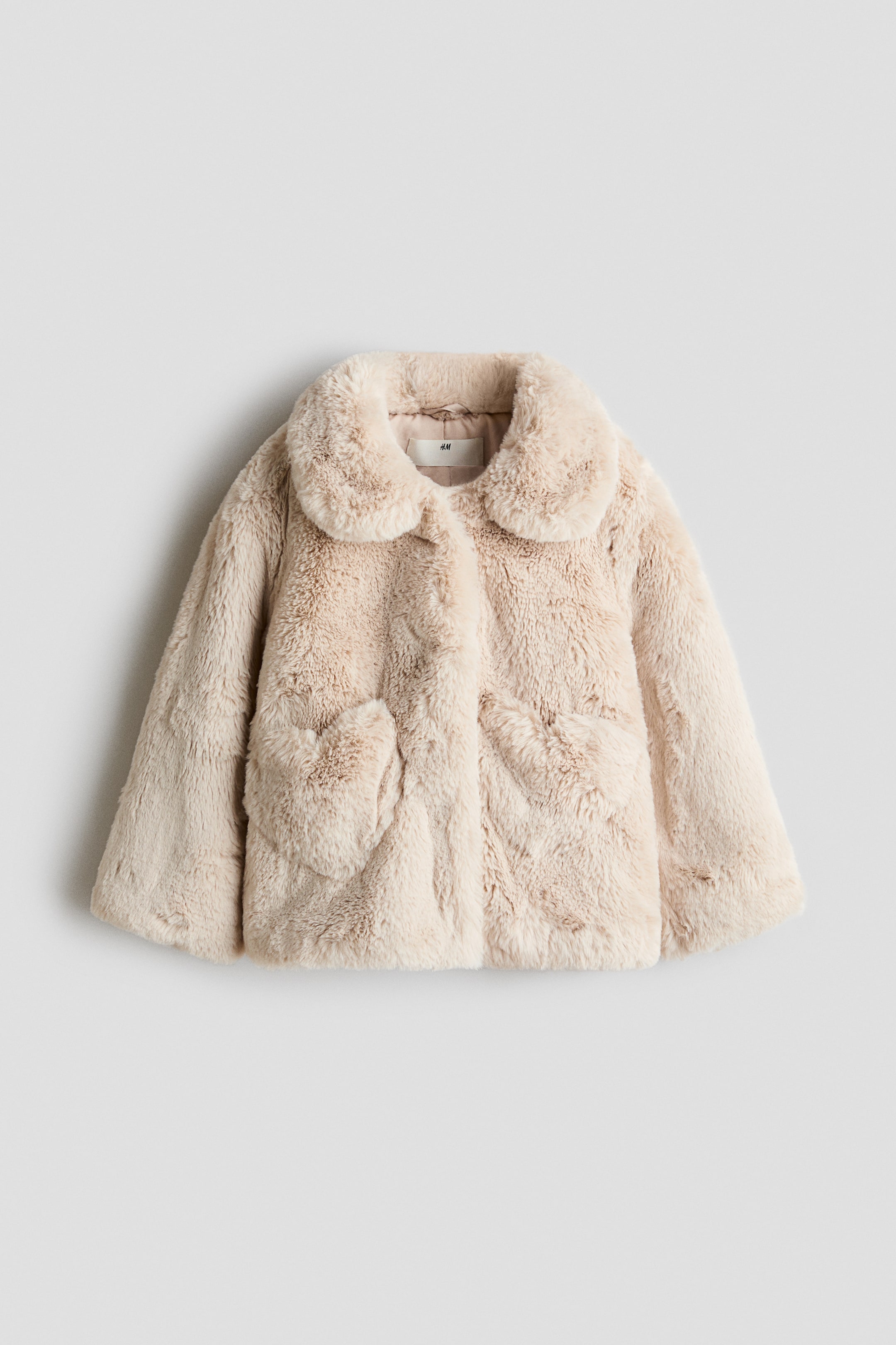 View larger image: A light beige faux fur jacket is facing forward, featuring a rounded collar, a button closure, and two large rounded patch pockets. The entire garment displays a shaggy, plush texture.