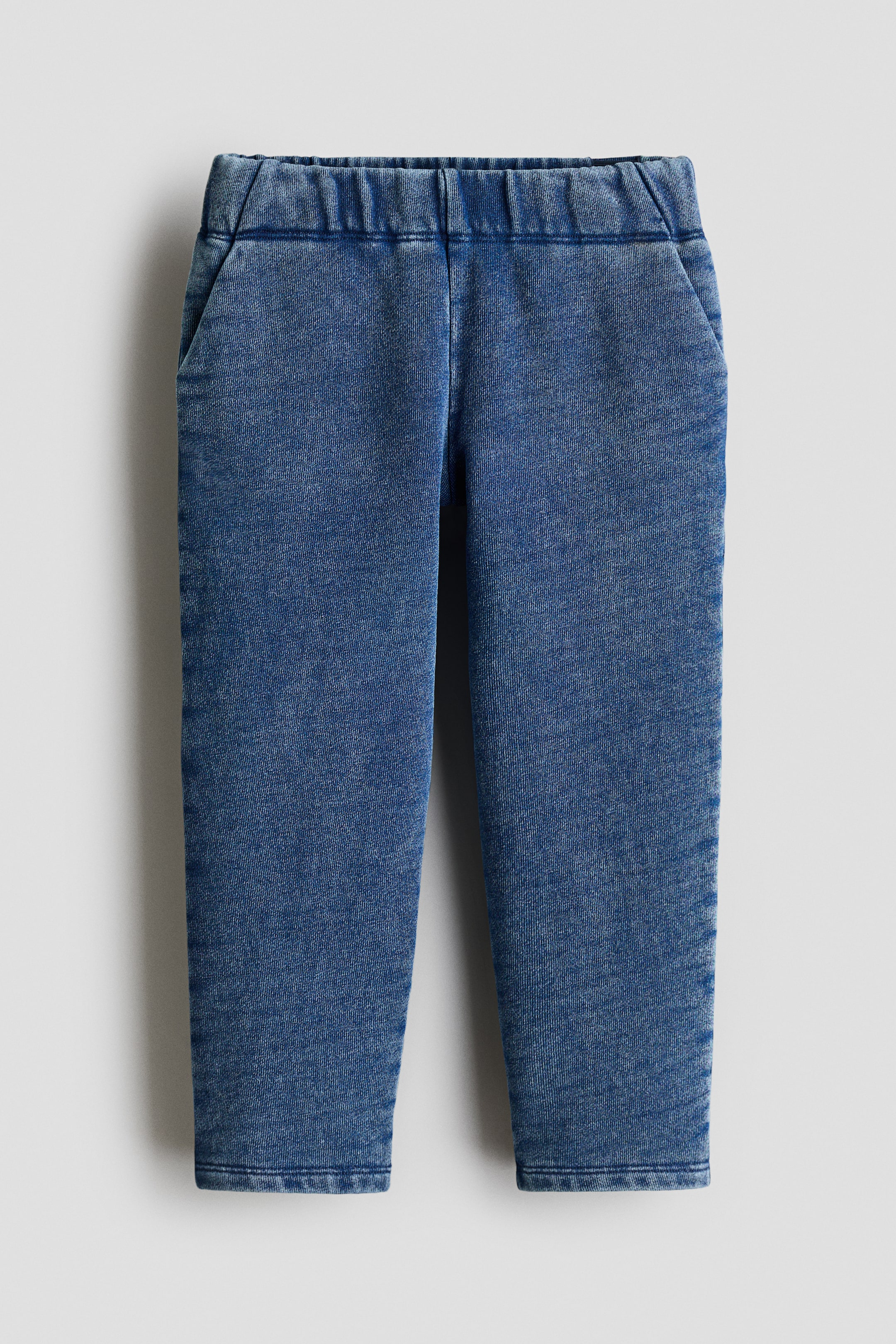 View larger image: H&M Adorables denim-look sweatshirt joggers are presenting from the FRONT, featuring an elasticated waistband and two diagonal side pockets. The blue fabric is displaying a washed effect and tapered legs.