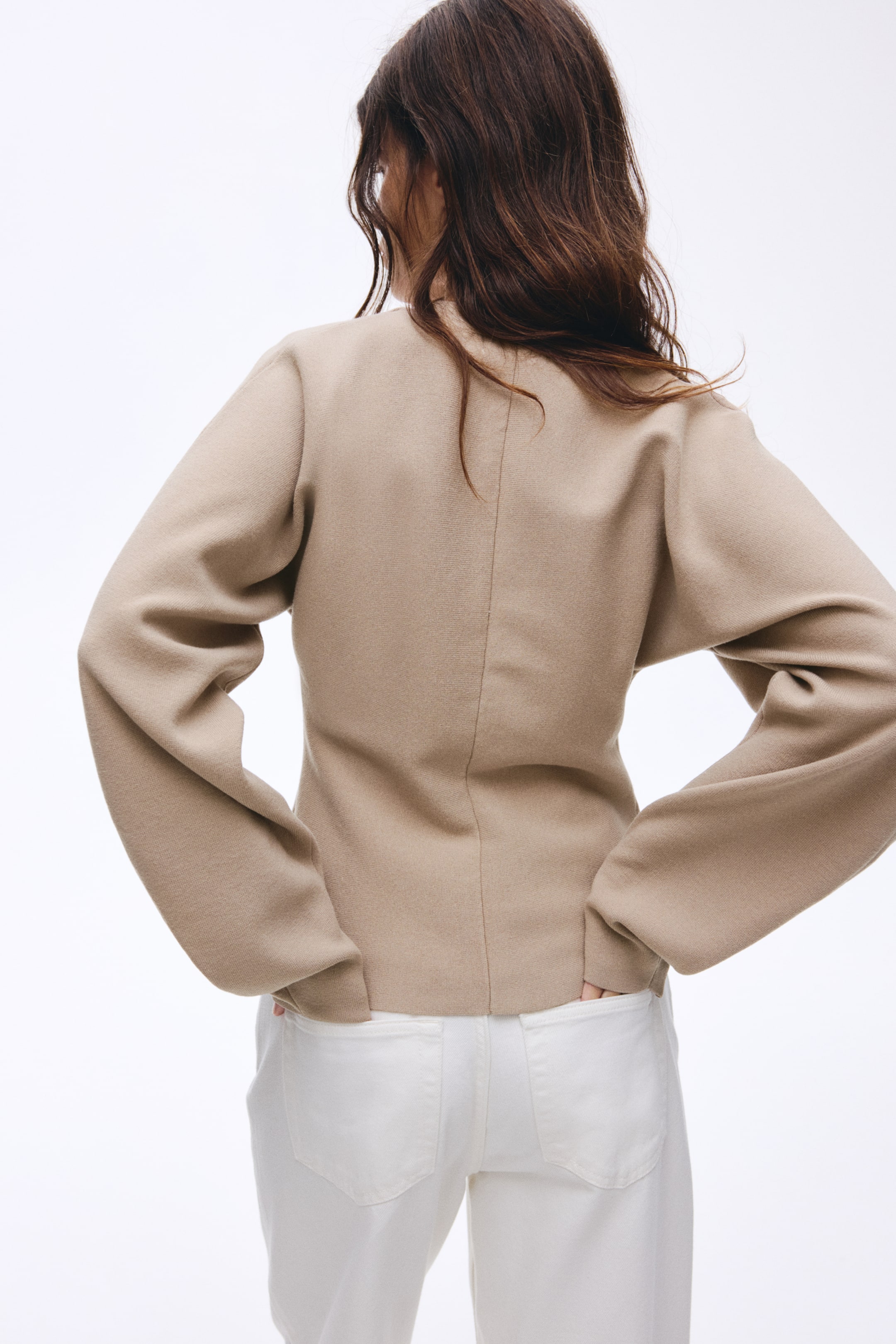 Agrandir l'image: Une veste beige est présentée de dos, avec des manches larges et légèrement volumineuses et un ourlet court qui se termine juste au-dessus d'un jean blanc. Une couture verticale parcourt le centre du dos.