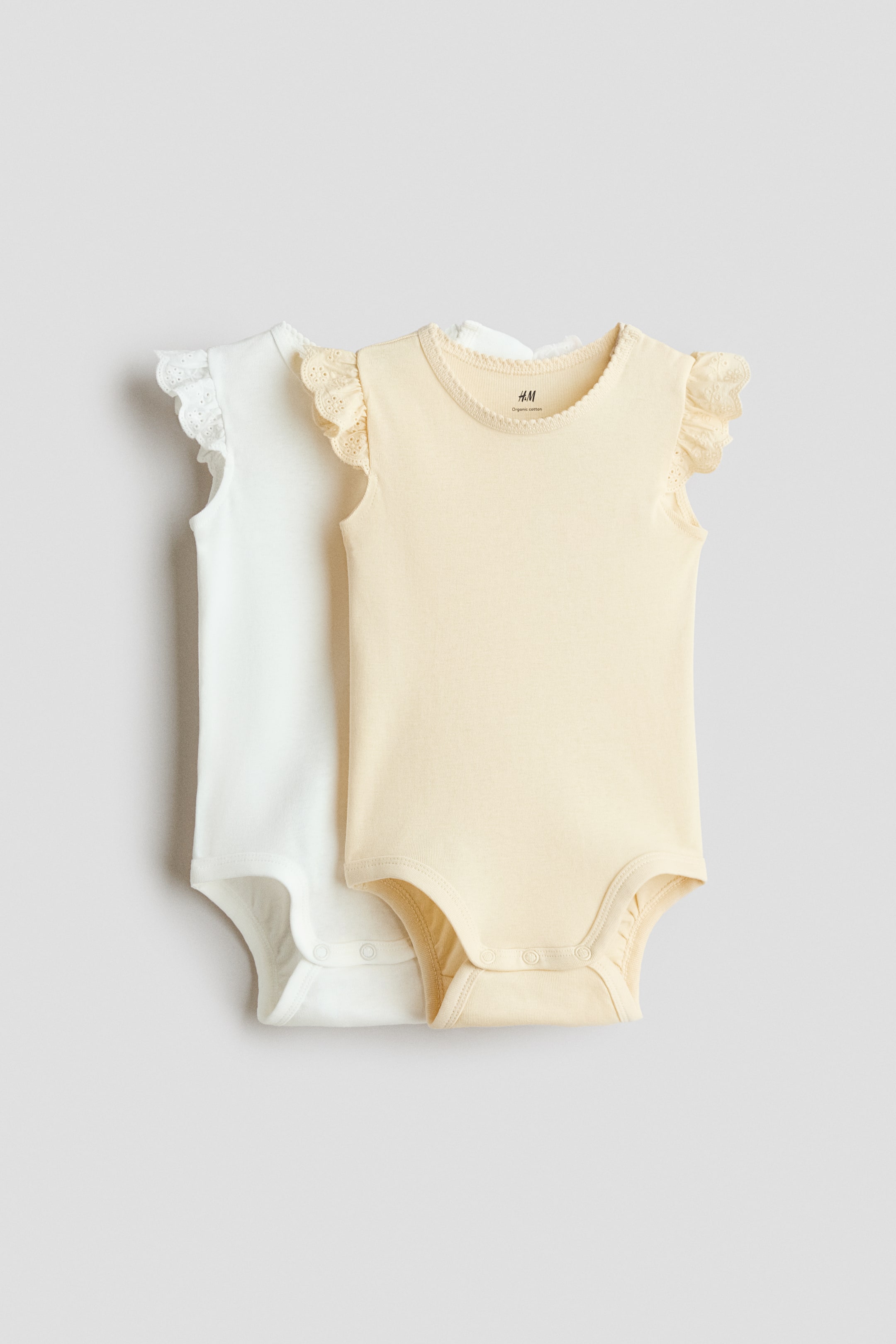 View larger image: Two baby bodysuits are showcased front-facing, one in yellow and the other in white. The yellow bodysuit features a round neckline with picot trim, ruffled cap sleeves adorned with eyelet lace detailing, and snap fasteners at the crotch, while it slightly overlaps the white bodysuit, which displays similar details.