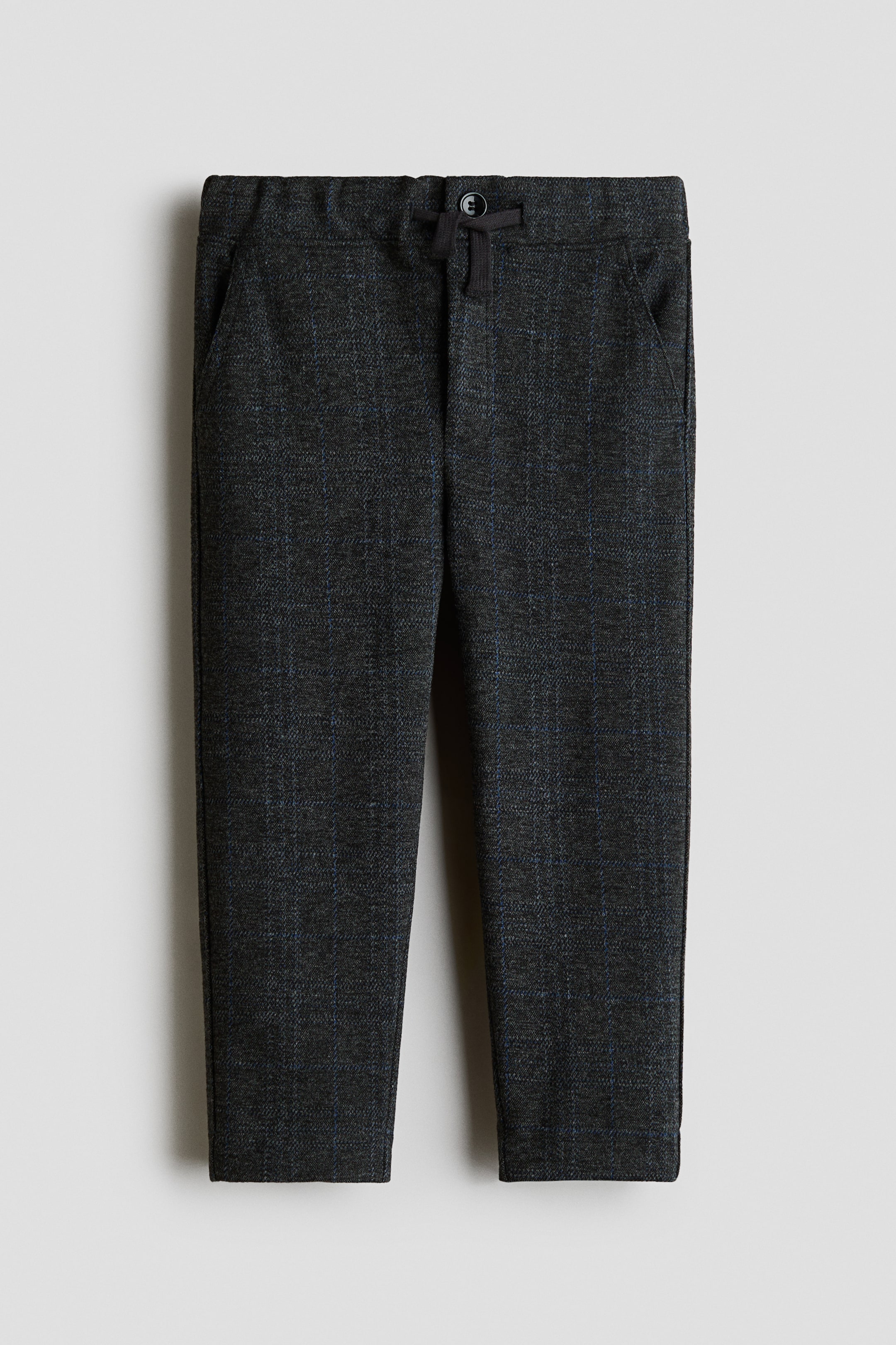 Grösseres Bild ansehen: Die Hose ist von vorne ausgerichtet und zeigt einen dunkelgrauen Stoff mit dezentem blauem Fensterkaro-Muster. Vorne ist ein elastischer Bund mit dunklem Kordelzug zu sehen, der mit einem kleinen dunklen Knopf befestigt ist, dazu zwei seitliche Eingrifftaschen sowie gerade Saumabschlüsse an den Beinen.