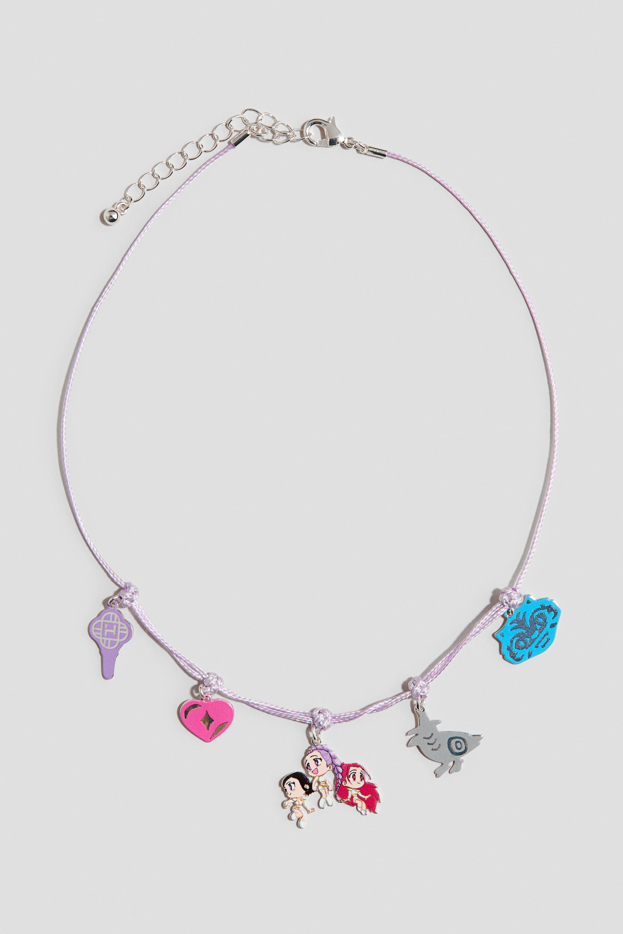 View larger image: A light purple cord necklace features five charms dangling along the front, attached by small knots. A purple key shape, a pink heart, three cartoon-style figures, a grey stylised animal, and a blue abstract shape are visibly attached to the cord. A silver-toned lobster clasp and extender chain complete the necklace at the back.