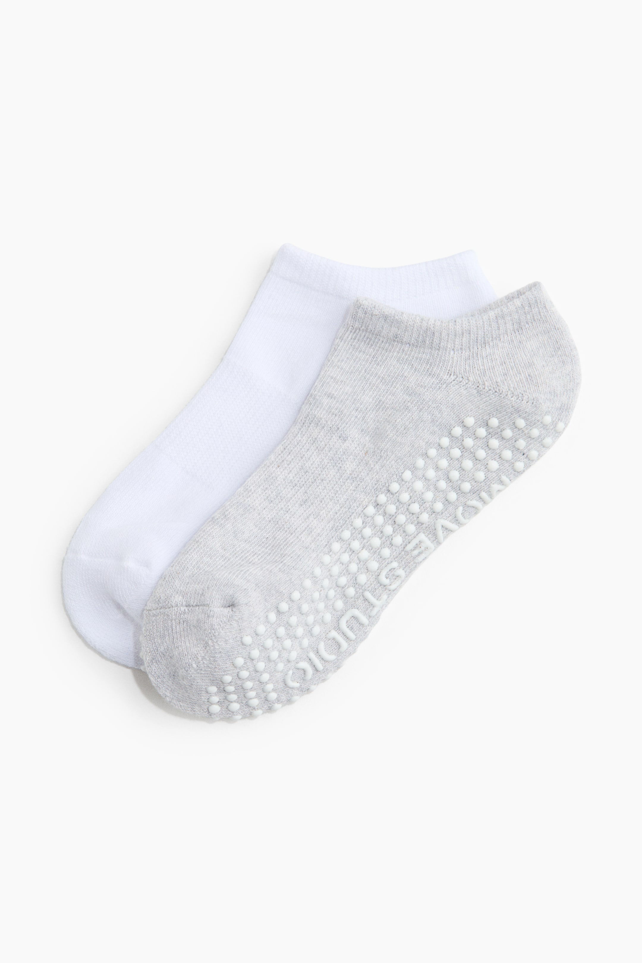 View larger image: A pair of ankle socks is displayed, with a white sock lying beneath a light gray sock. The gray sock's sole is facing upwards, showcasing white anti-slip grips that form the text "MOVE STUDIO." Both socks feature ribbed cuffs.
