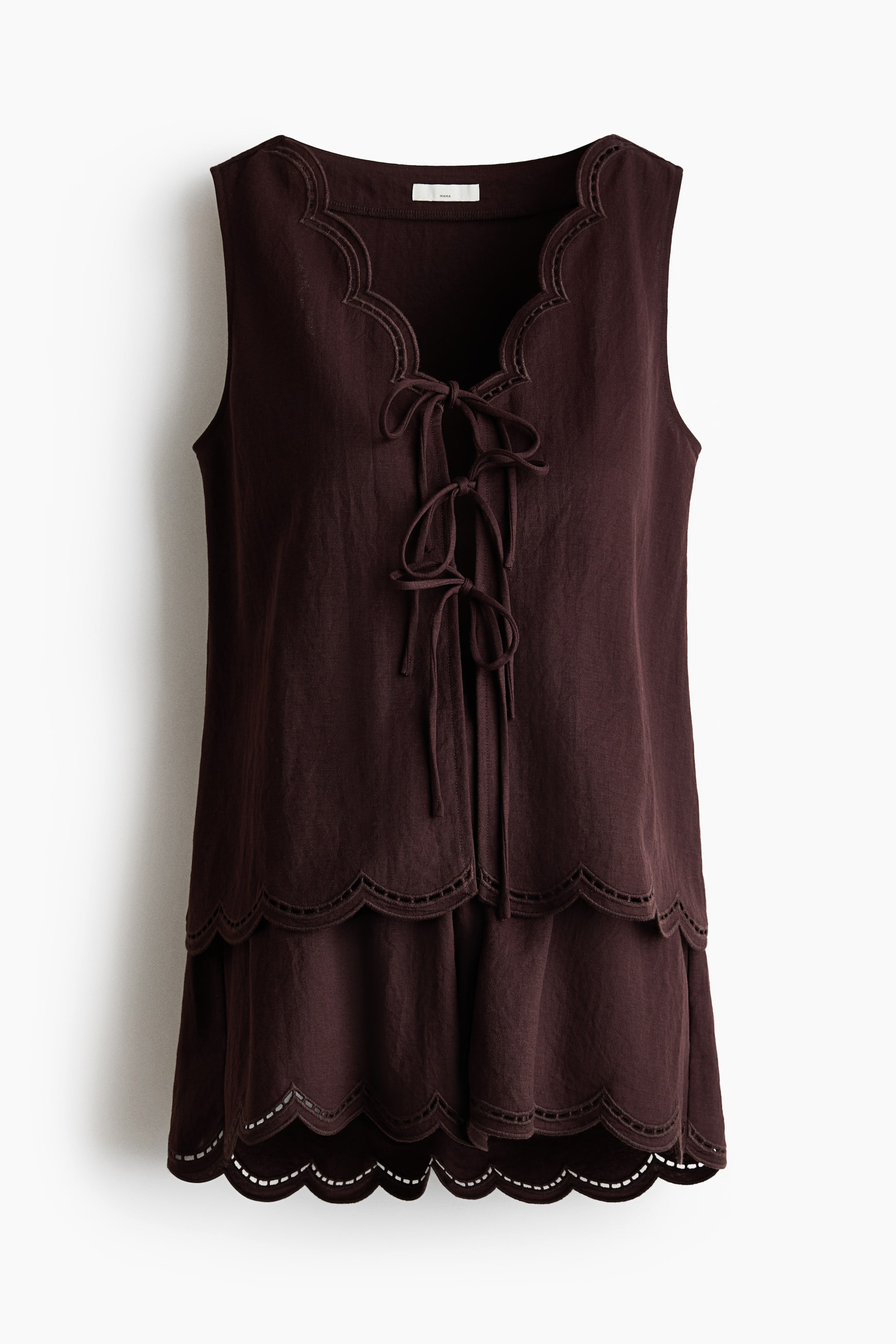 View larger image: A dark brown woven set is shown from the front, featuring a sleeveless top and shorts. The top highlights a deep V-neckline with scalloped broderie anglaise trim and an open front secured by three sets of narrow ties. Both the top's lower hem and the shorts' hems feature scalloped broderie anglaise, with the shorts also having a small frill trim at the waist.
