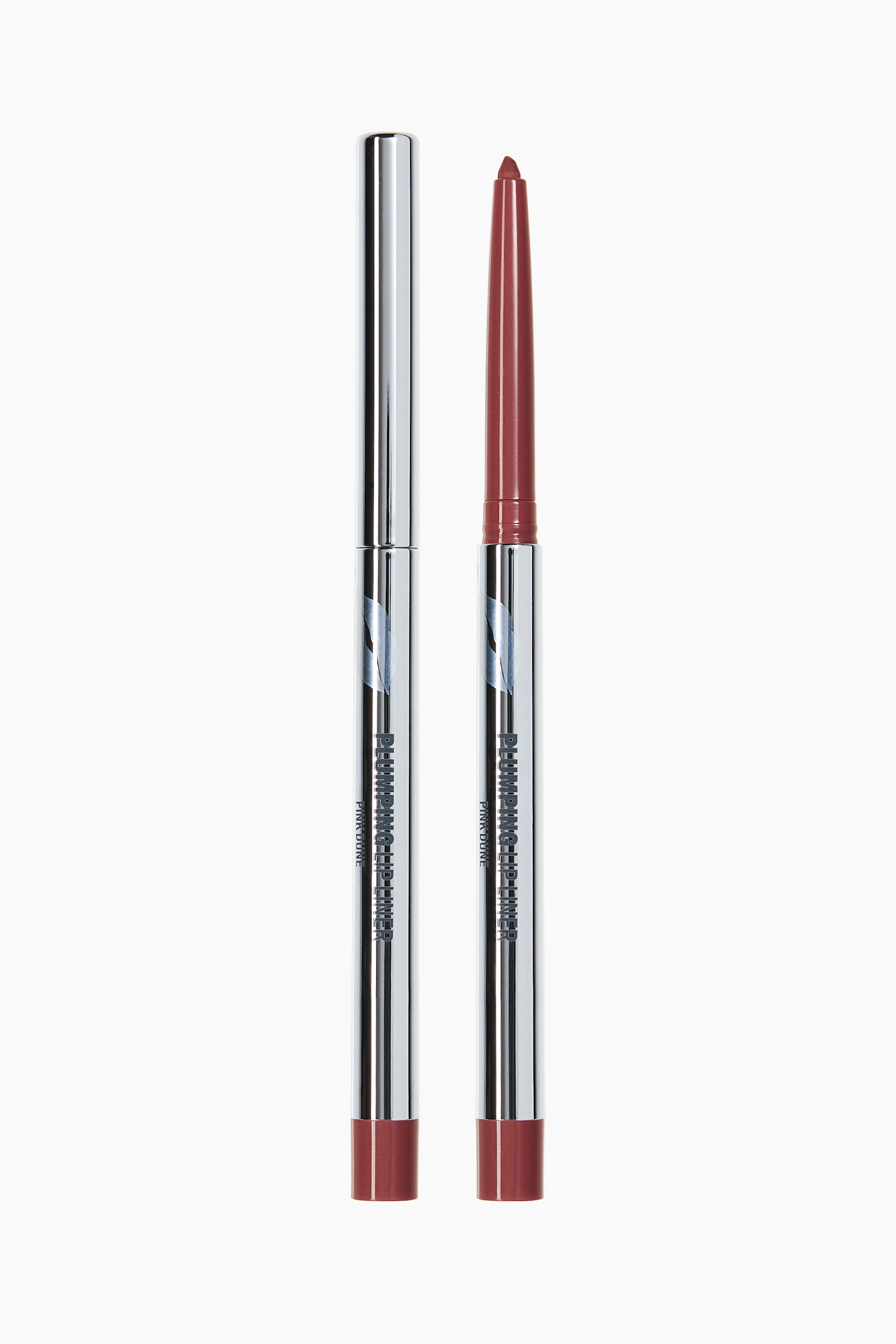 View larger image: Two lip liners are standing upright, facing forward, each showcasing a sleek, metallic silver body with the text "PLUMPING LIP LINER" and "PINK DUNE" visible, along with a reddish-brown color band at the base. One liner is capped with a metallic silver top, while the other is uncapped, displaying a pointed, reddish-brown lip liner tip.