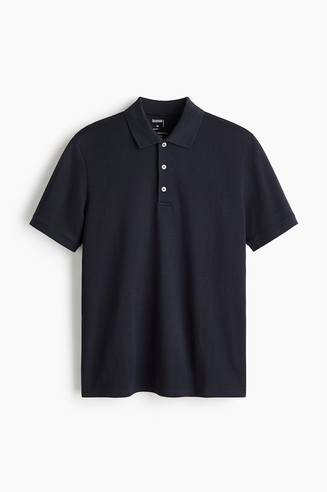 A dark navy polo shirt is hanging in a front-facing view, featuring a classic collar, a three-button placket with white buttons, and short sleeves with trimmed cuffs. The shirt is displaying a regular fit and a straight-cut hem. - 1