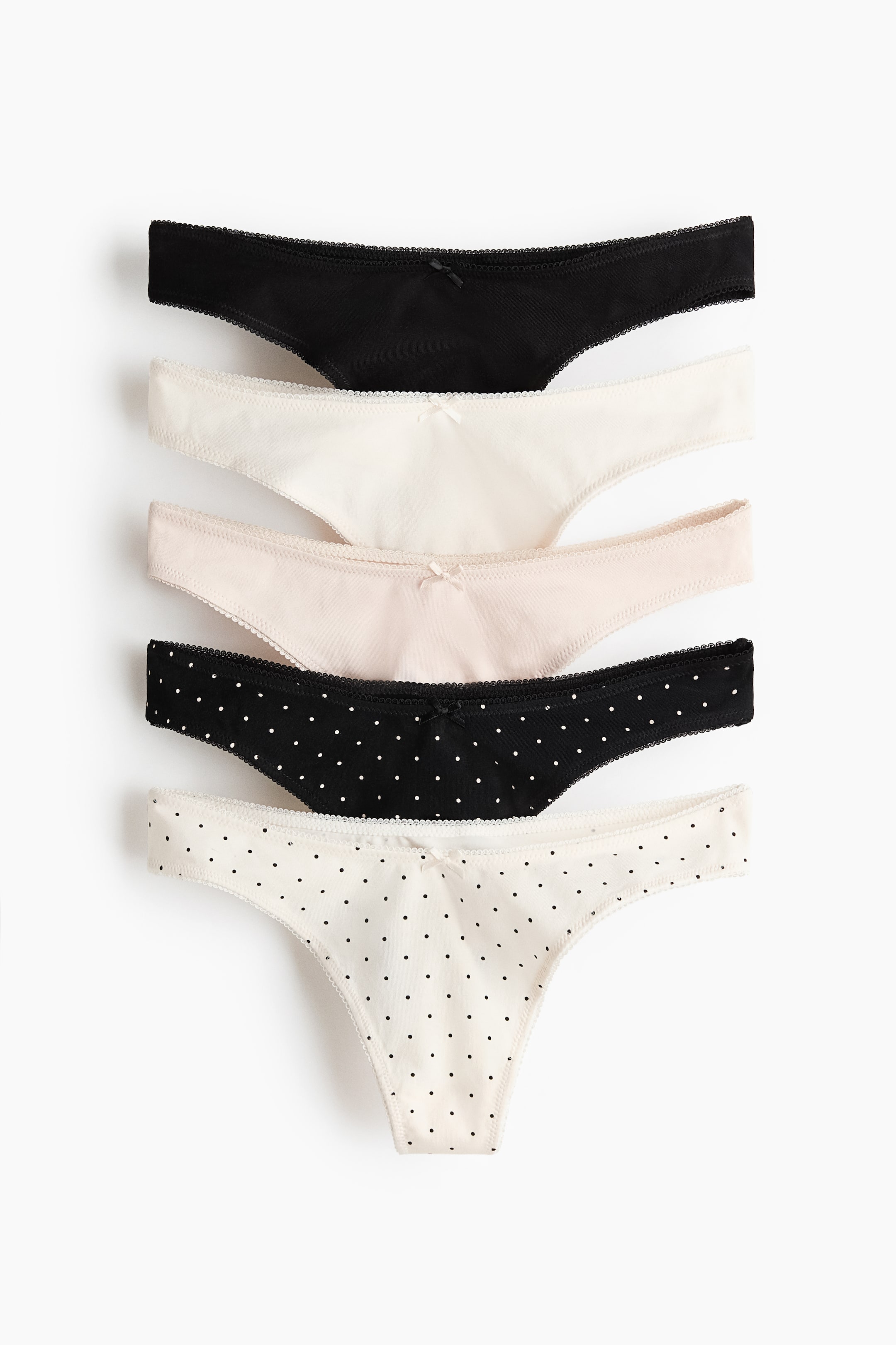 View larger image: Five cotton jersey thong briefs are lying FRONT, each featuring a low, V-shaped waist, a small bow at the center front waistband, and delicate scalloped trim along the edges. They are presented in solid black, solid cream, solid light pink, black with white polka dots, and cream with black polka dots.