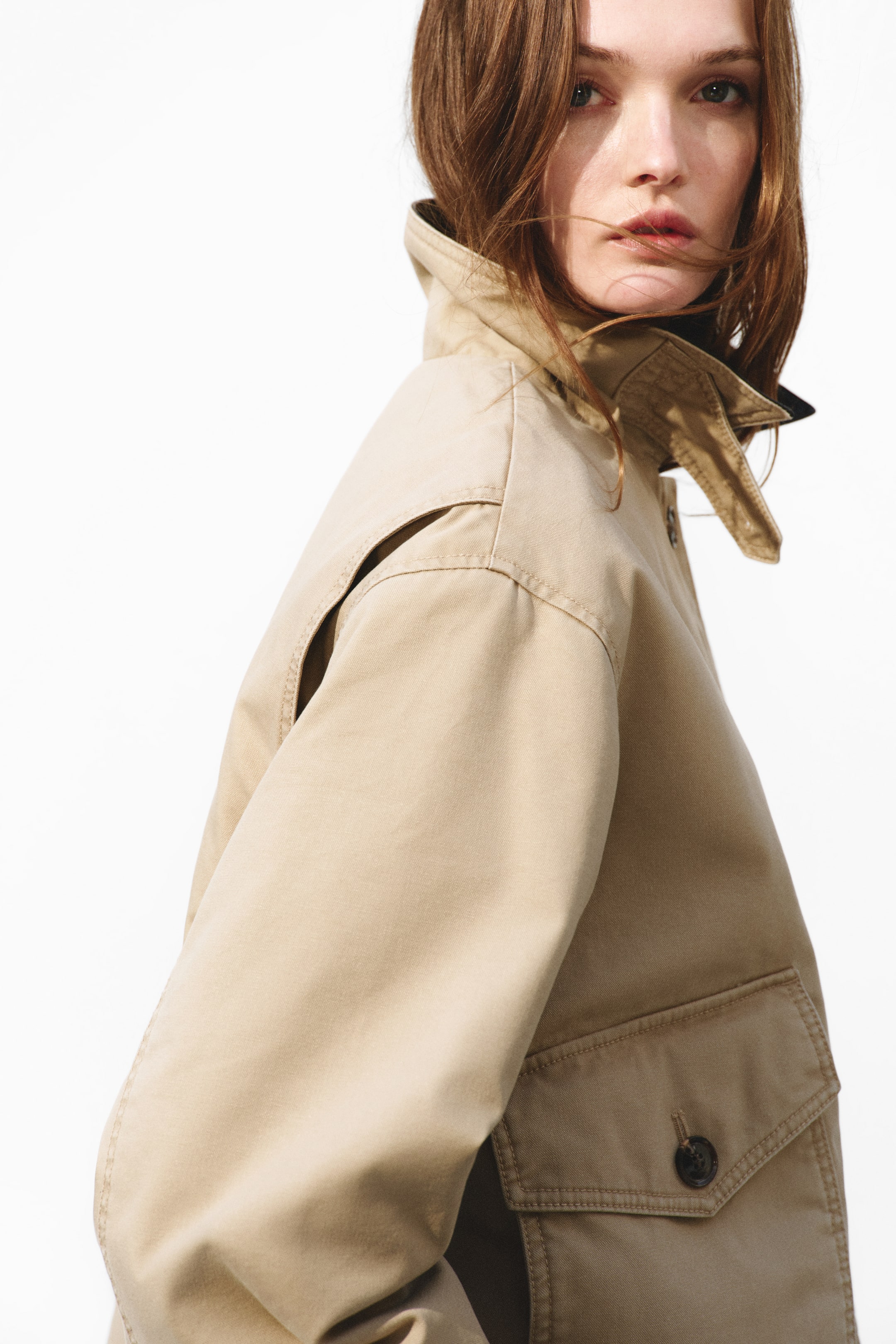 Visa större bild: En beige jacka med ståkrage och mörkare innerfoder, axelklaff och en ficka med lock och mörk knapp på nedre högra sidan, sedd från en sned framvinkel.