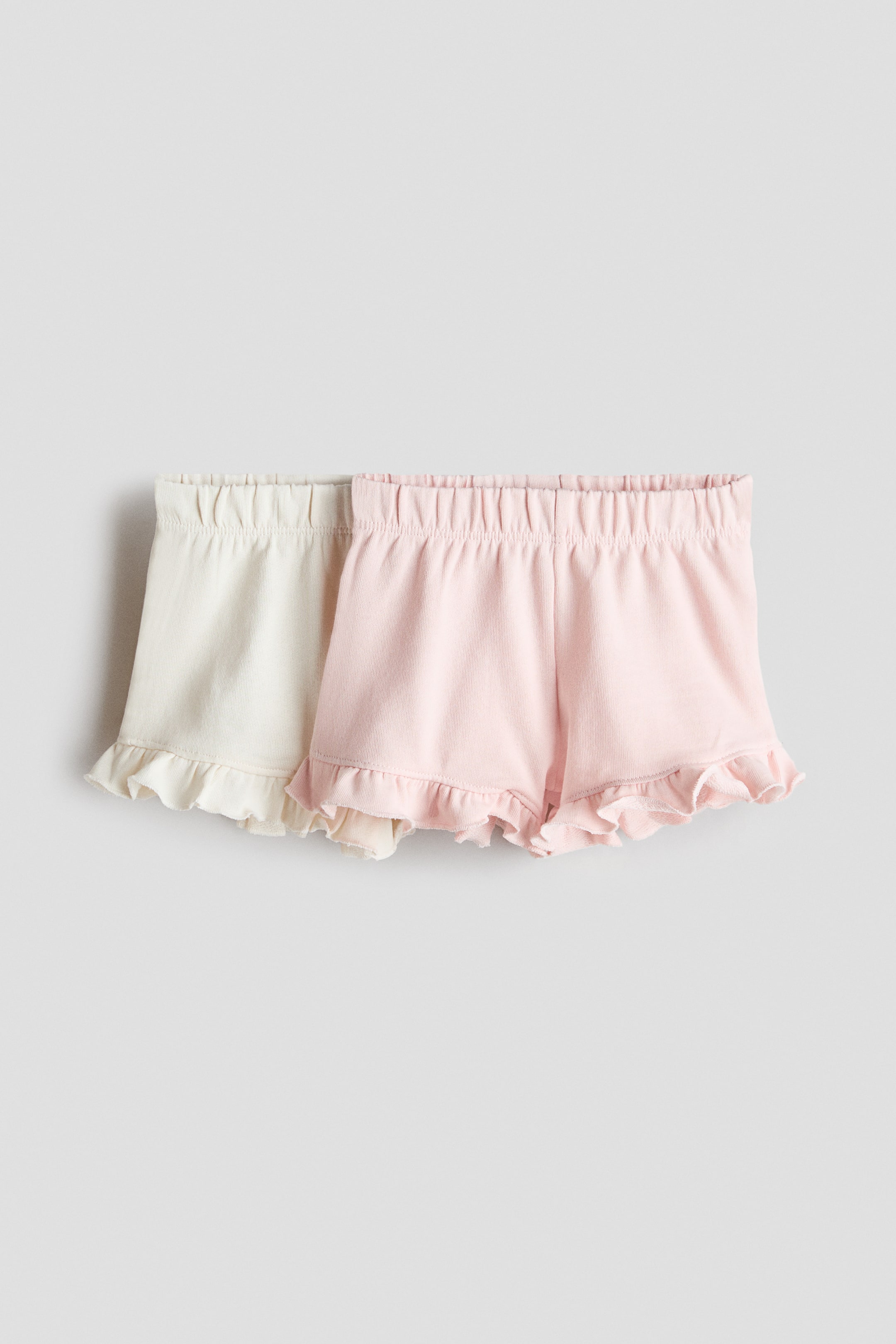 View larger image: A set of two pairs of shorts showcases an off-white pair and a light pink pair, both designed with elasticated, gathered waistbands and ruffled leg openings, displayed from a front-facing angle.