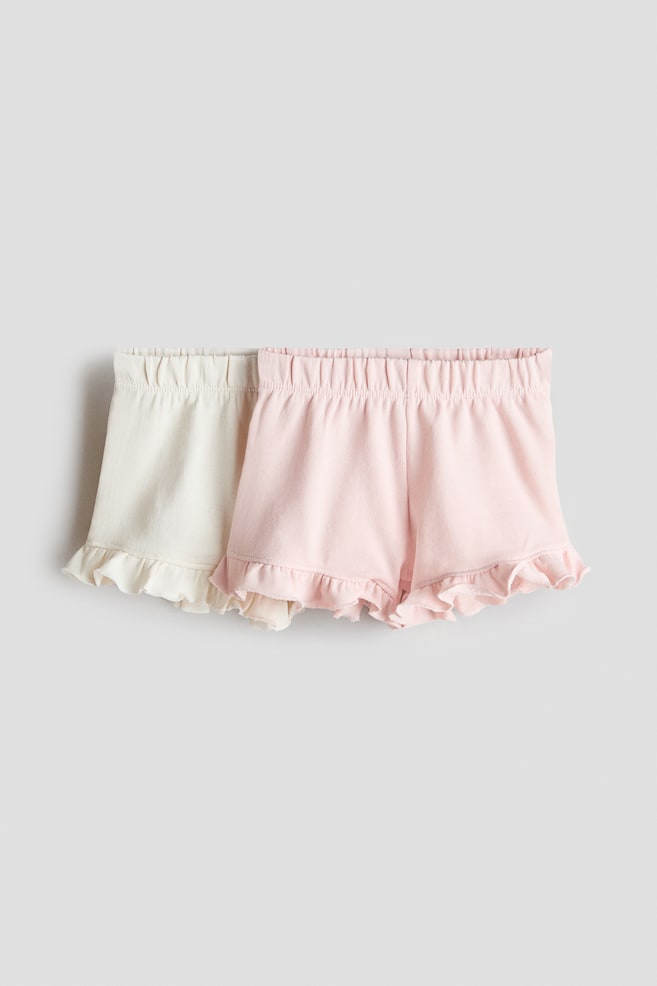 A set of two pairs of shorts is featuring an off-white pair and a light pink pair, both with elasticated, gathered waistbands and ruffled leg openings, presented from a front-facing angle. - 1