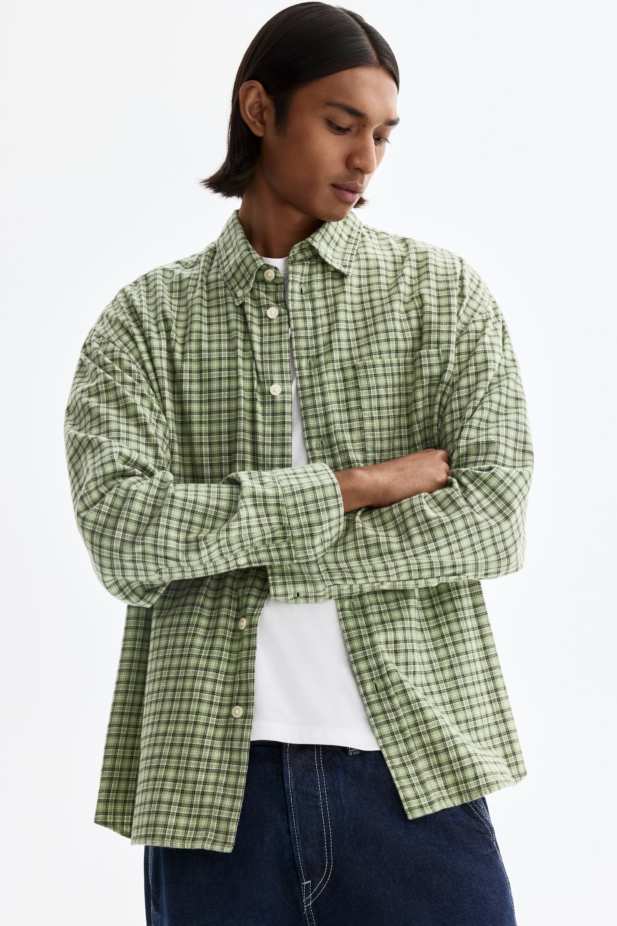 View larger image: A green plaid shirt features a button-down collar and light-coloured buttons along the front placket. It is cut in a relaxed fit, worn open over a white T-shirt, and has long sleeves with buttoned cuffs.