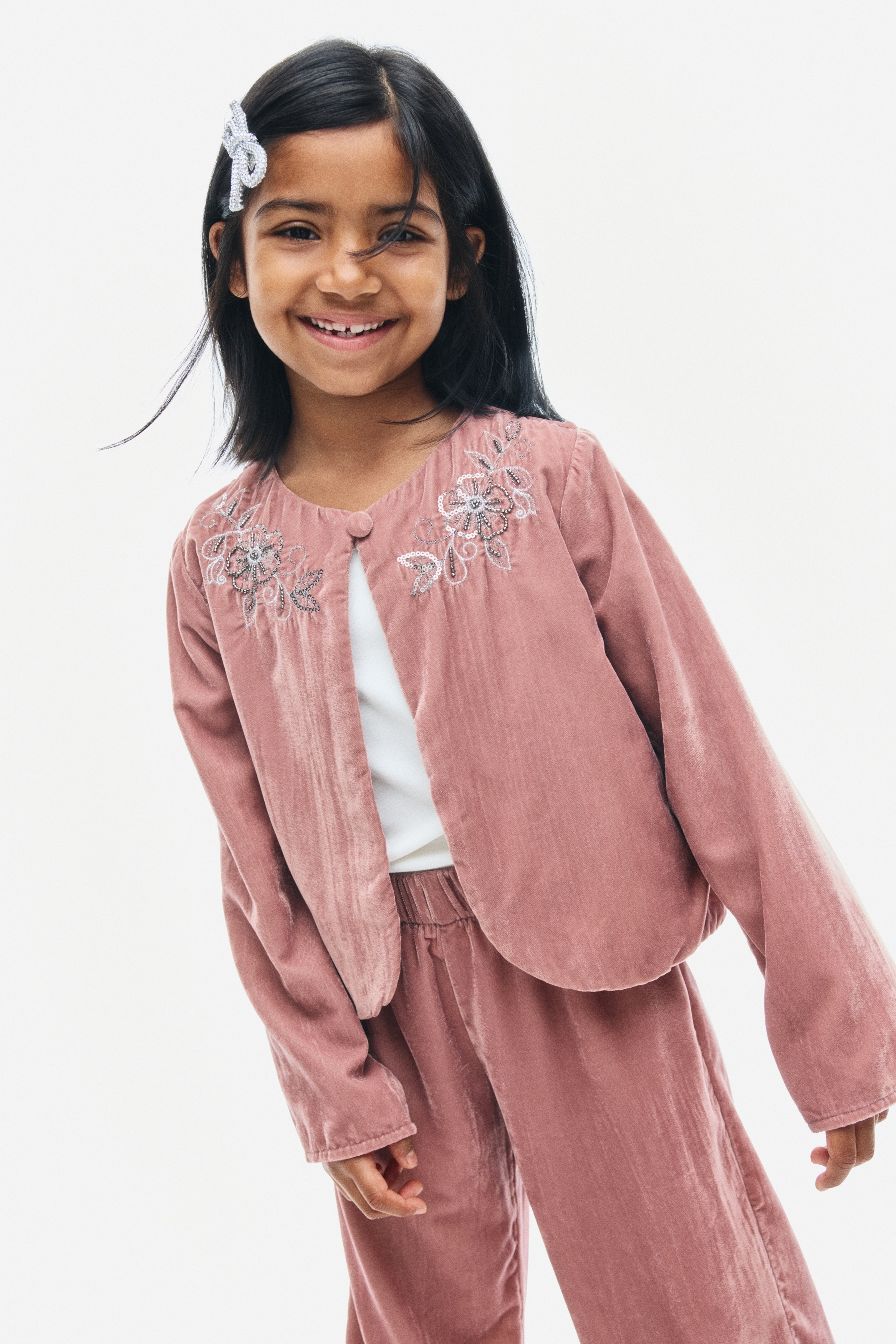 A front-facing dusty pink crinkled velvet jacket featuring long sleeves and a round neckline with a single covered button fastening. Intricate floral embroidery with metallic beads embellishes both sides of the upper chest.