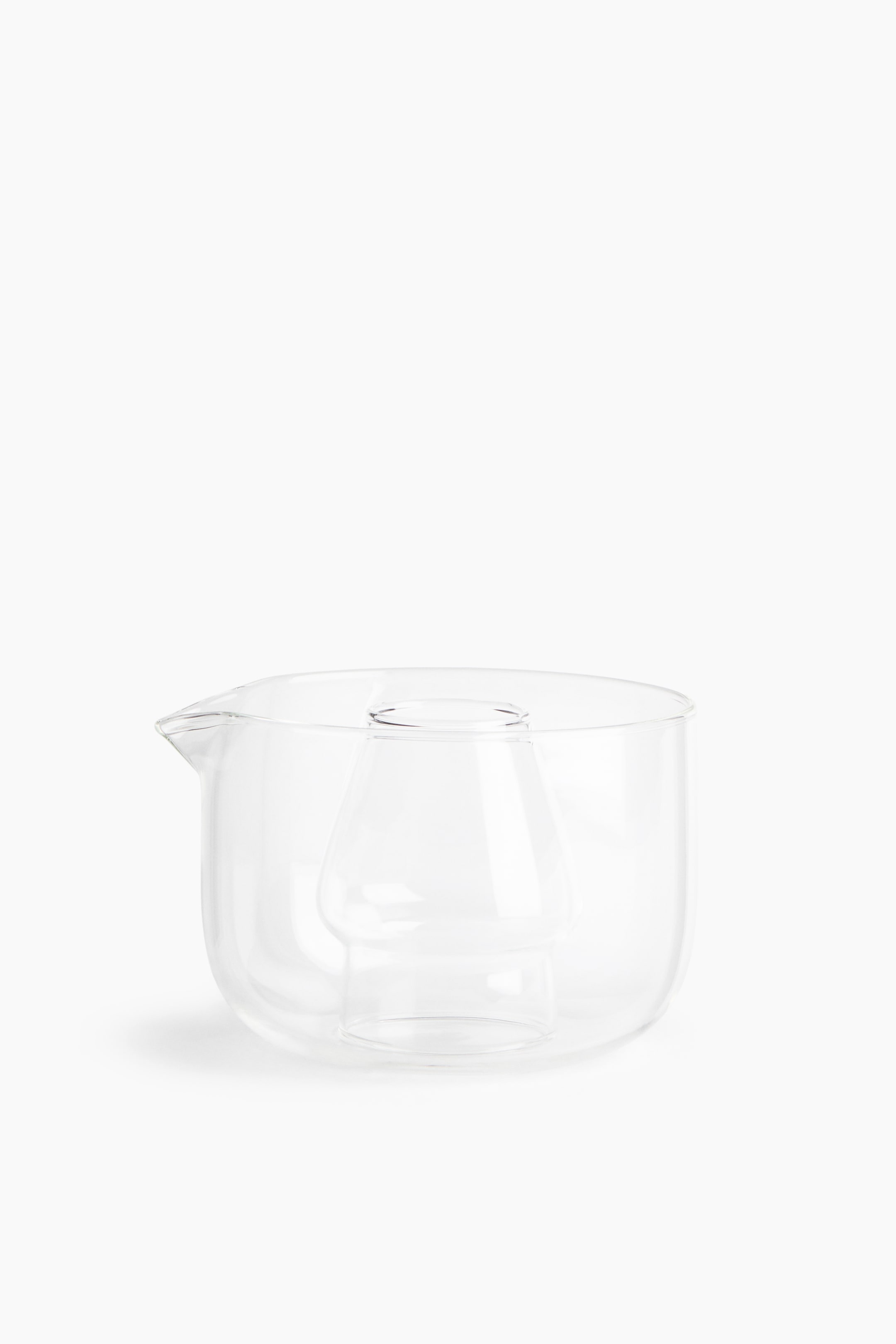 View larger image: A clear glass server is positioned facing forward, featuring a wide cylindrical body with a small pouring spout on the left rim. An integrated hollow glass chamber rises from the centre of the base, creating a separate compartment inside the vessel.