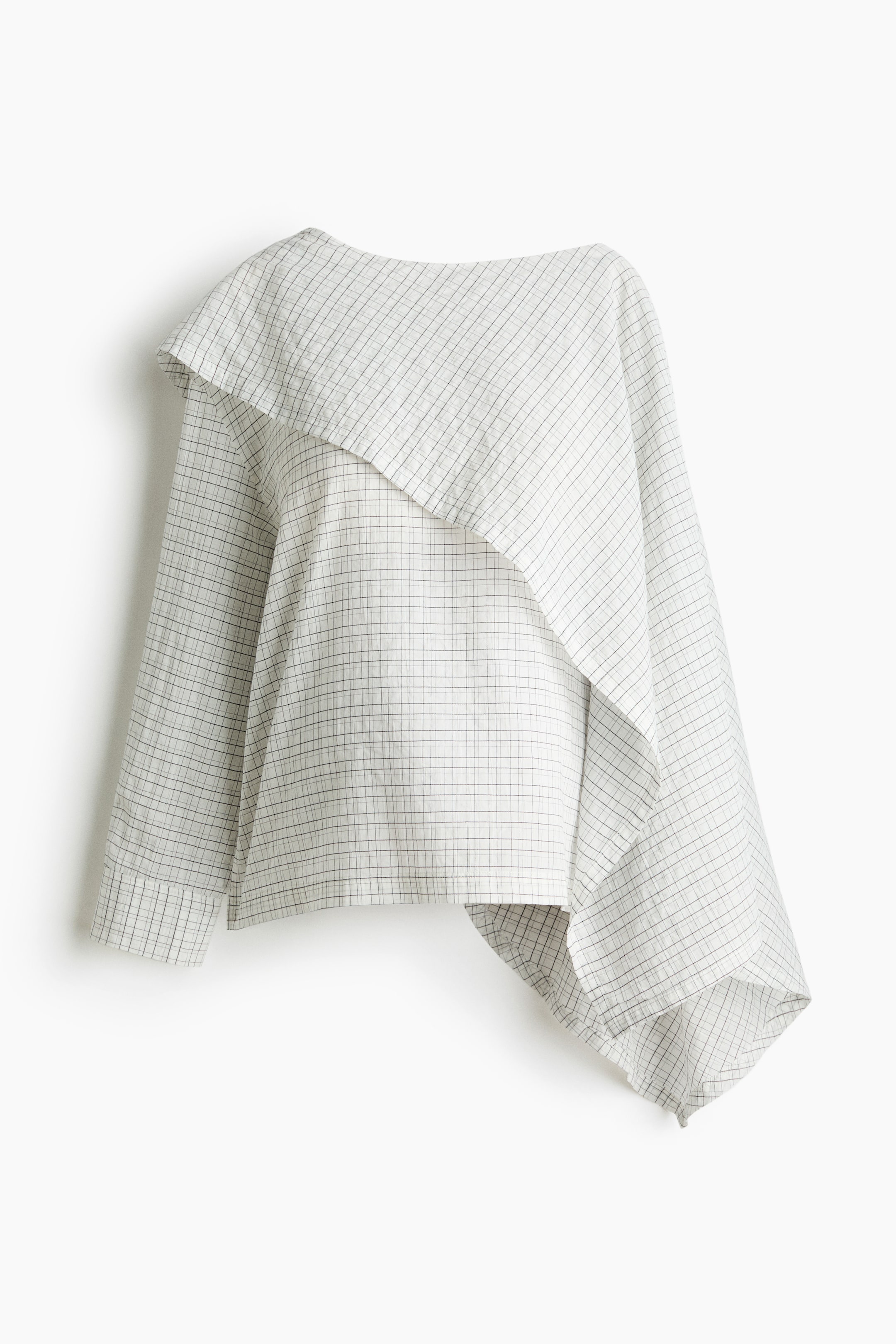 View larger image: A white and dark checkered seersucker blouse is displayed from the front, showcasing an asymmetric cape-style layer draped across the top. It also features long sleeves with buttoned cuffs and a straight-cut hem with side slits.