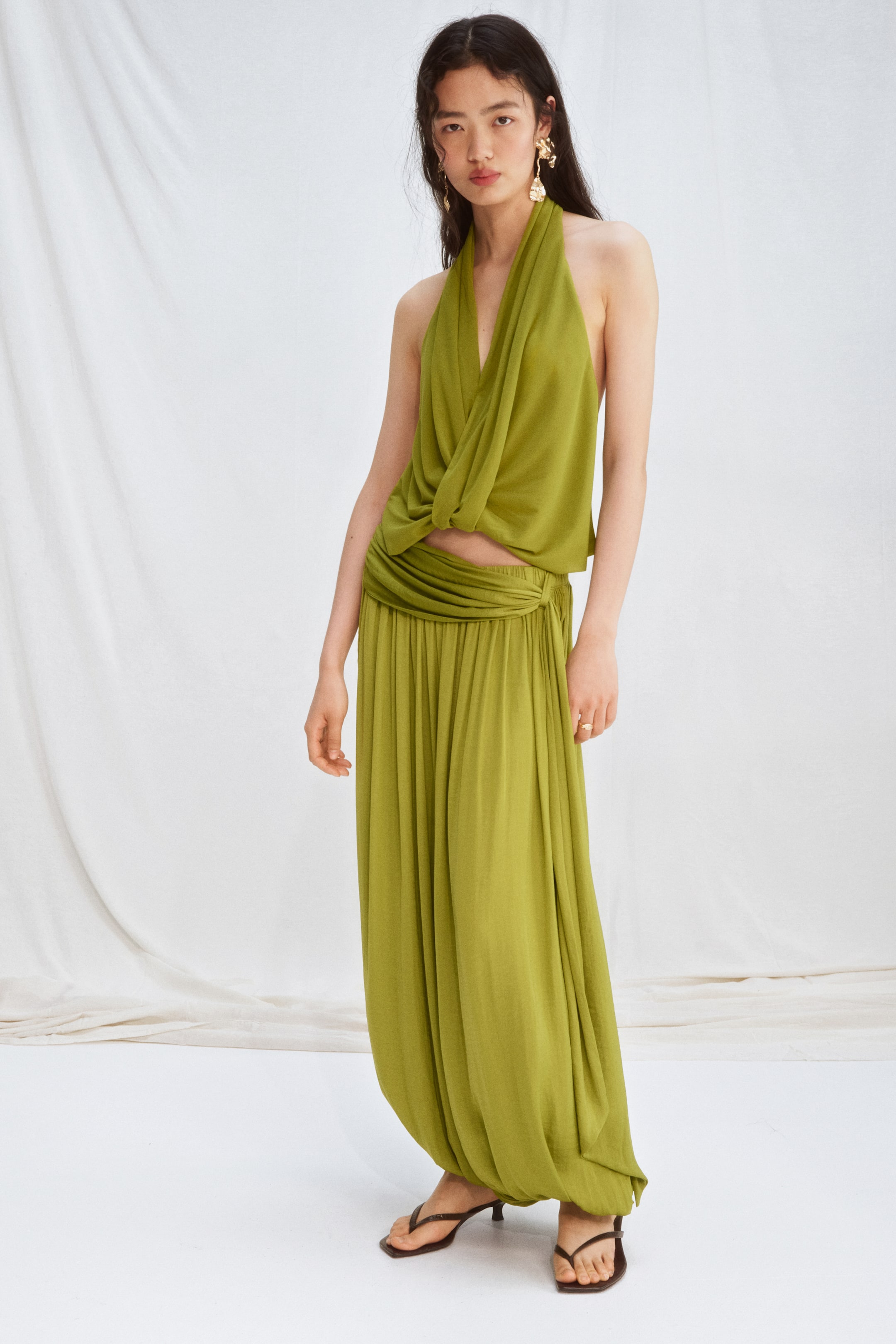 Größeres Bild ansehen: Knöchellange, locker sitzende Hosen aus weich fließendem Satin werden vom Model getragen. Sie zeigen einen elastischen Bund mit einem drapierten Panel, das einen asymmetrischen, geschichteten Effekt erzeugt, sowie Ballonbeine mit verdecktem Gummizug an den Säumen.