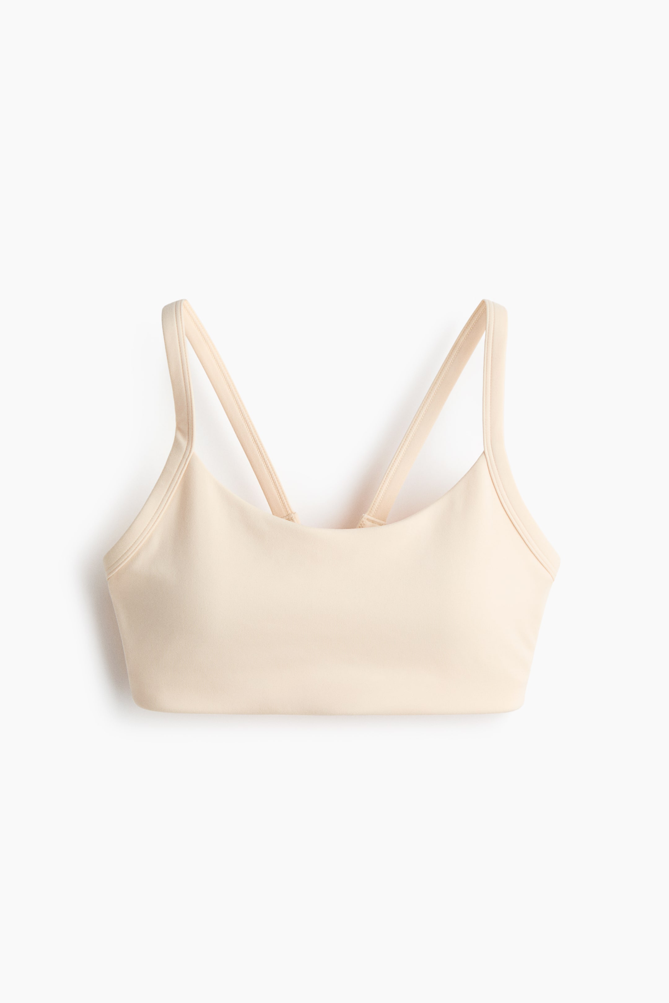 View larger image: A medium-support sports bra with SoftMove is shown from the front, appearing in a light beige colour. It features a scoop neckline, narrow shoulder straps angling upwards and inwards to suggest a cross-back design, and a smooth, matte fabric texture.