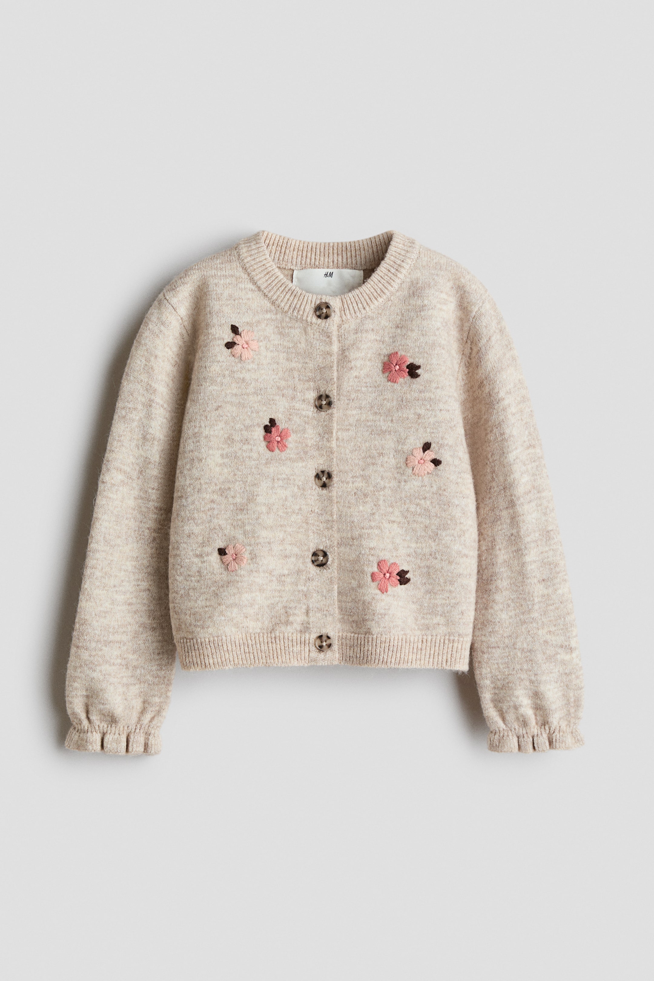 Voir une image plus grande: Un cardigan en tricot beige pâle est présenté de face, mettant en valeur un col rond côtelé, cinq fermetures à boutons foncés et des fleurs roses brodées disséminées, agrémentées de petites feuilles brunes. Les longues manches se terminent par des poignets à volants, et le vêtement est fini avec un ourlet côtelé.
