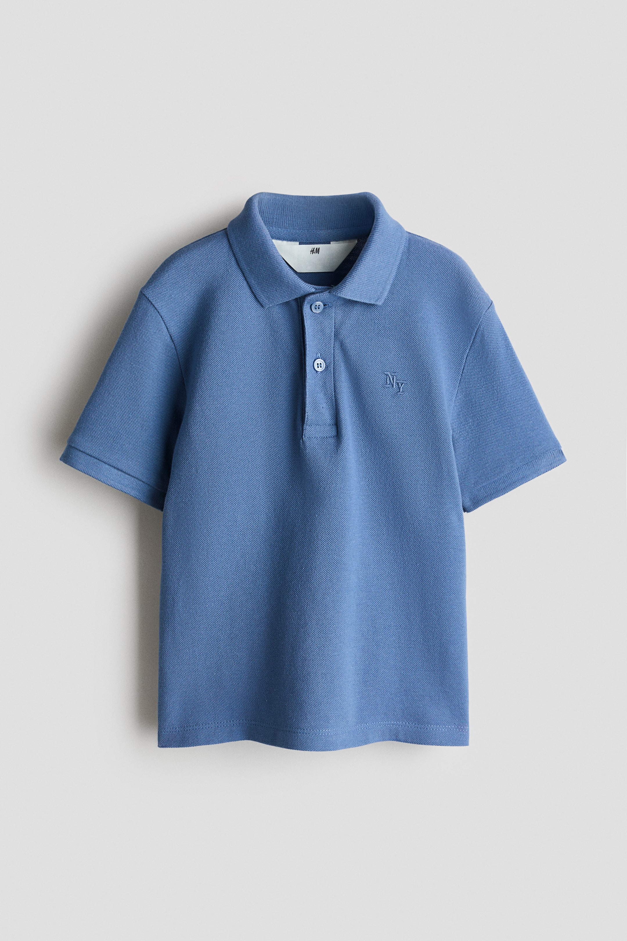 View larger image: A blue polo shirt is shown from the front, featuring a classic collar and a two-button placket with light-colored buttons. It displays short sleeves, a textured pique knit fabric, and a matching blue 'NY' embroidery on the left chest.
