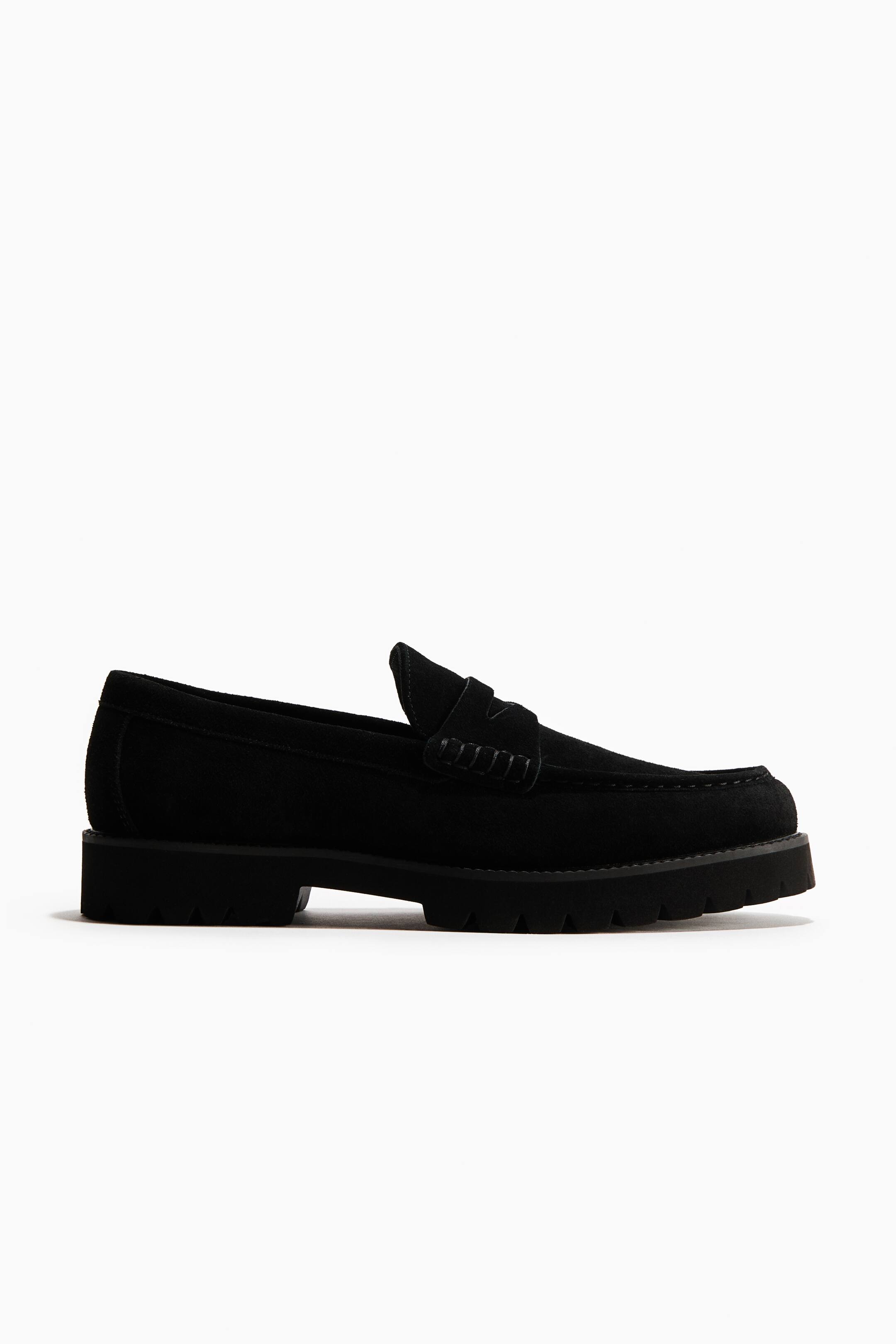 View larger image: A black suede penny loafer is facing right in a side profile. It is featuring a thick, lugged sole and a decorative strap across the vamp.